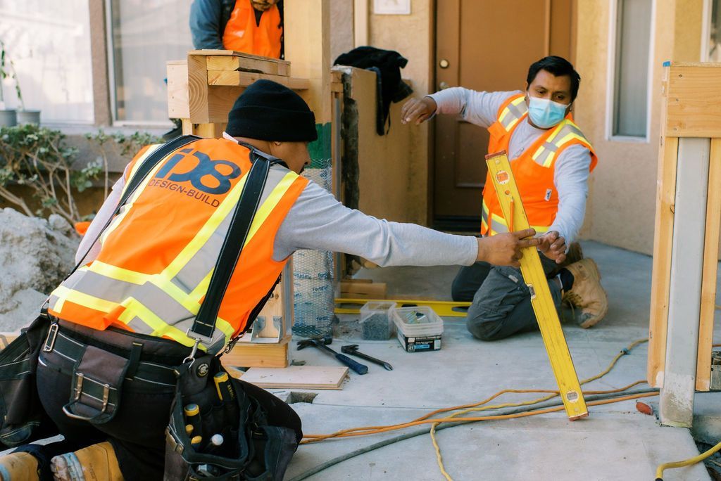 Two construction workers wearing safety vests and masks are working on a building.