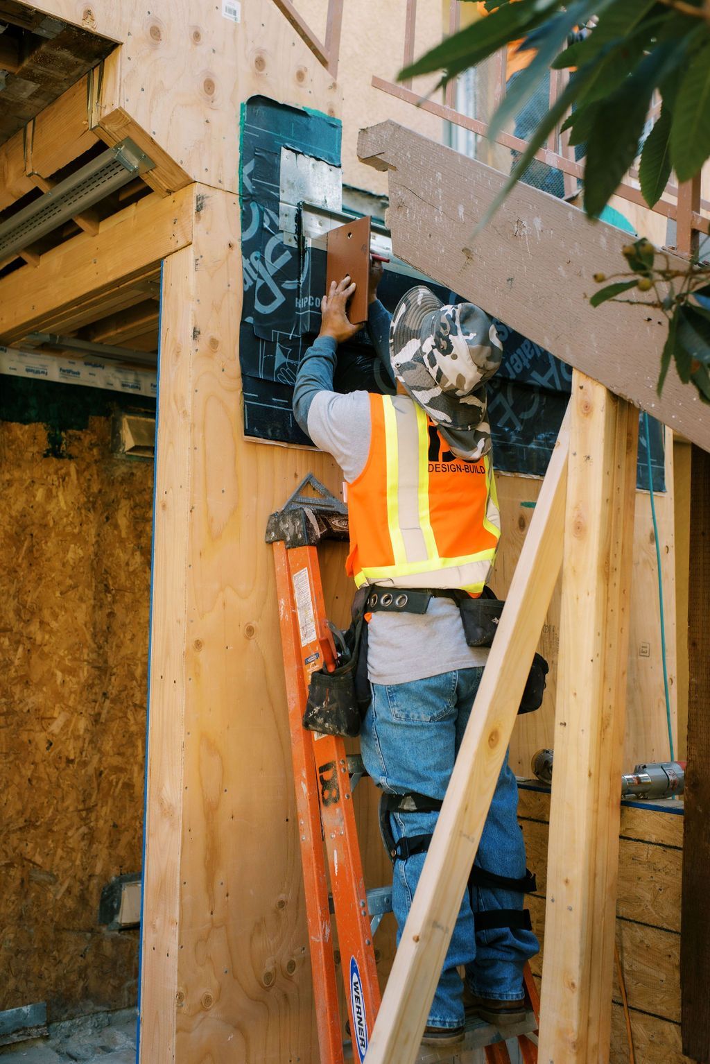 A construction worker is standing on a ladder working on a wall.