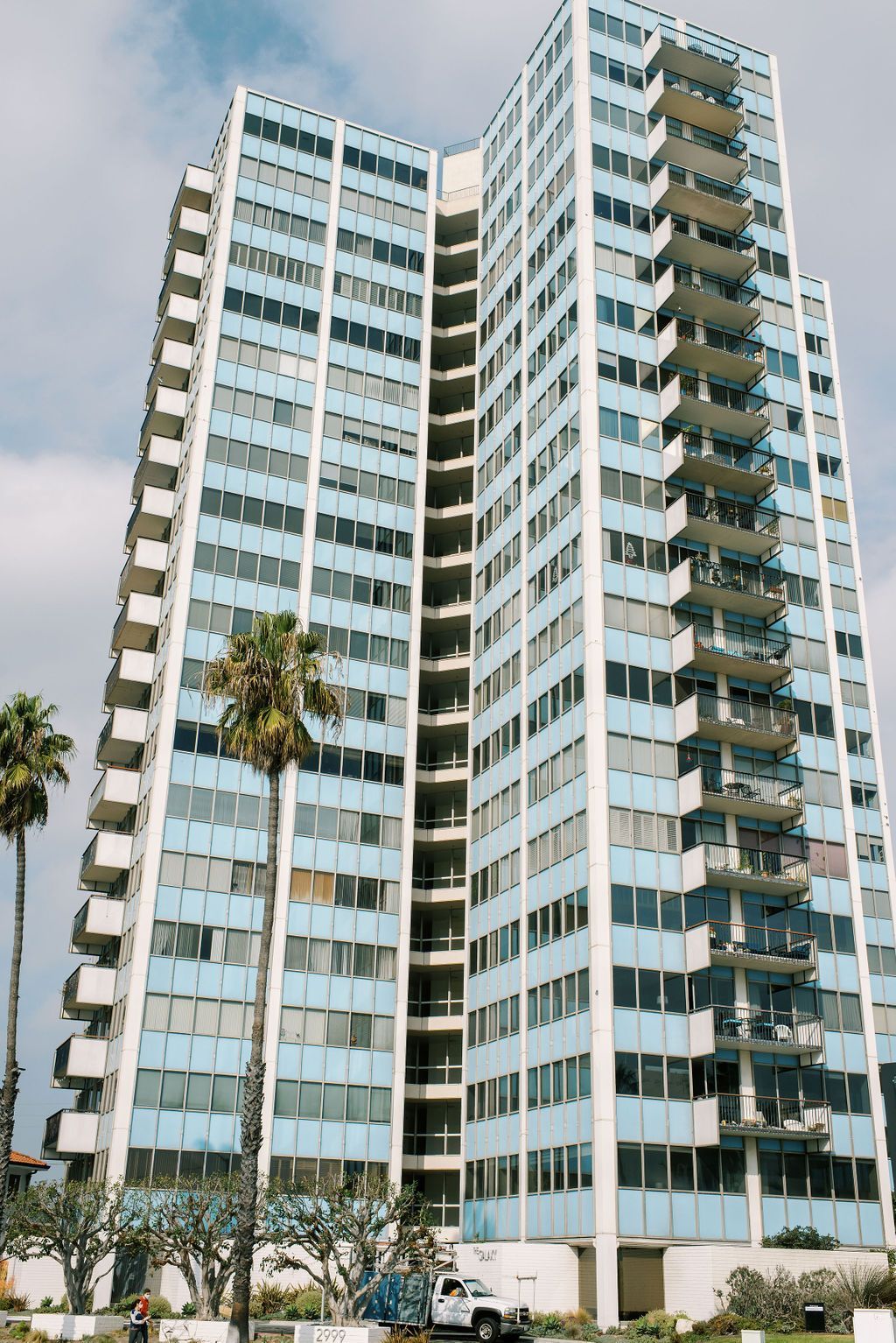 A tall building with a lot of windows is surrounded by palm trees.