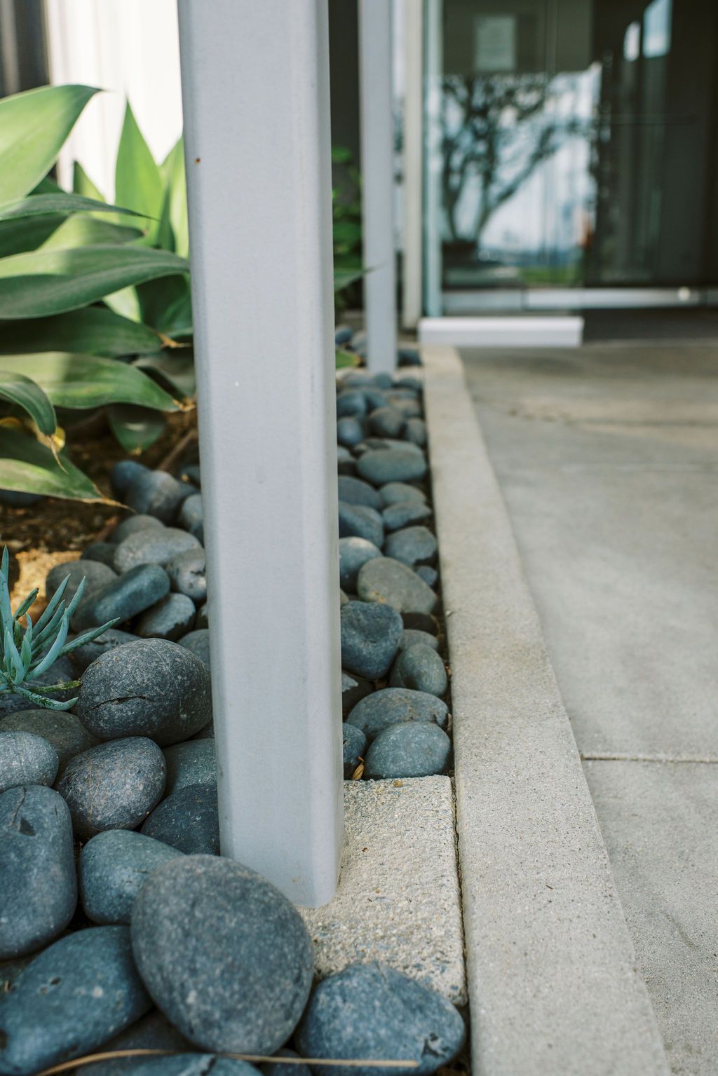 A row of rocks along a sidewalk next to a white pole.