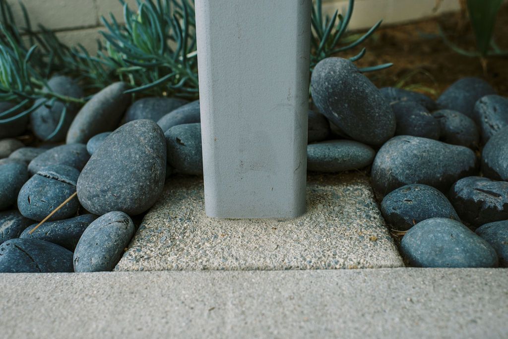 A concrete post is surrounded by rocks and plants.
