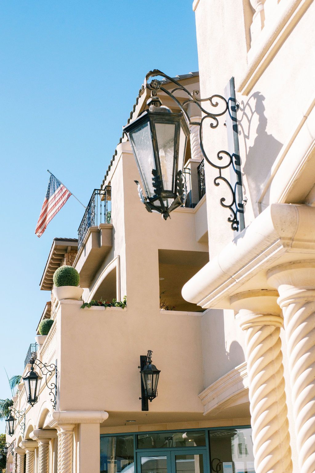 A building with a lamp hanging from the side of it and an american flag flying in the background.
