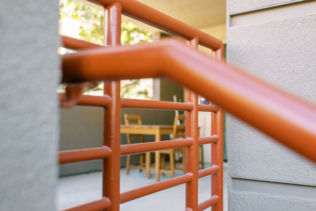 A red railing leading to a balcony with a table and chairs in the background