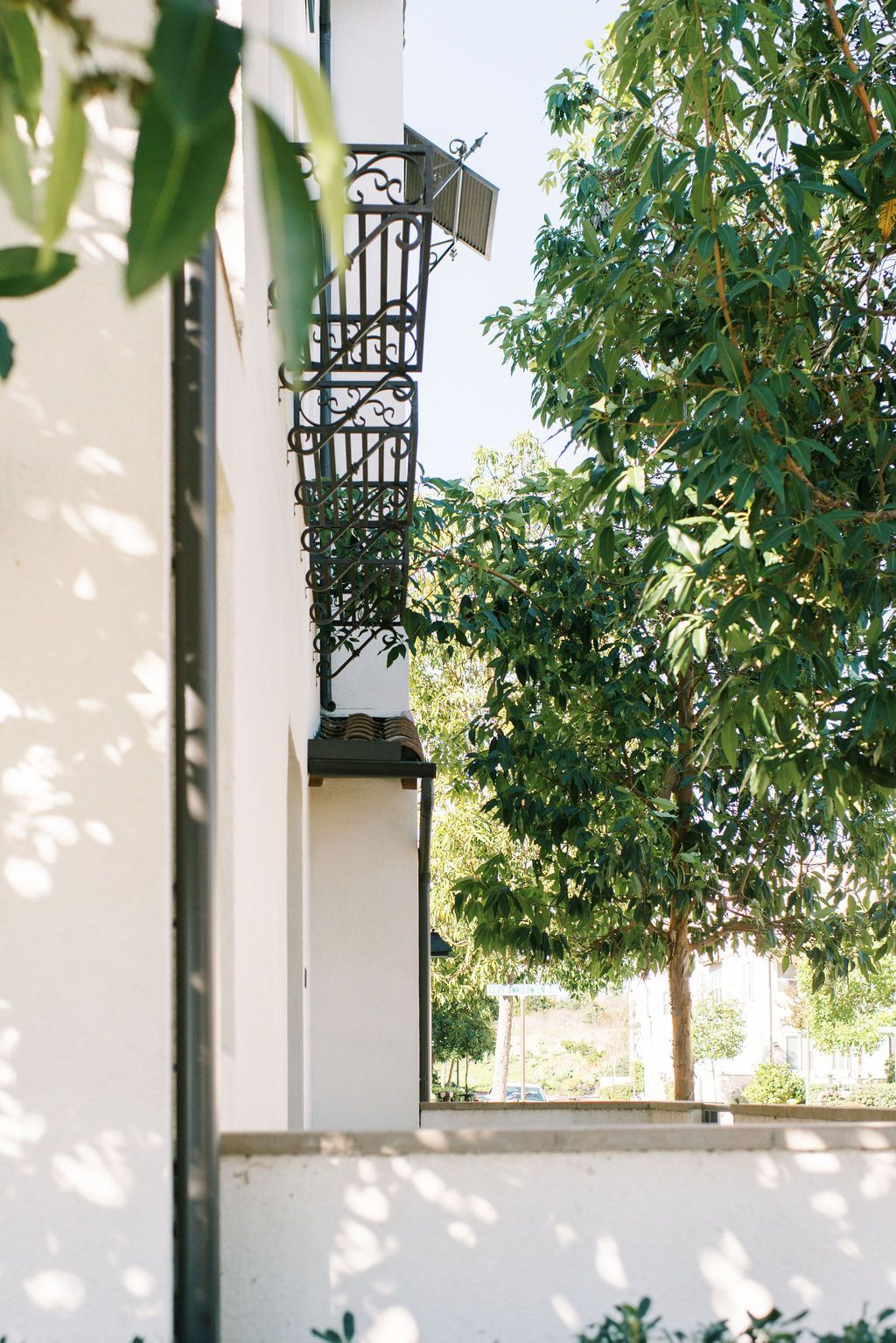 A white building with a balcony and a tree in front of it.