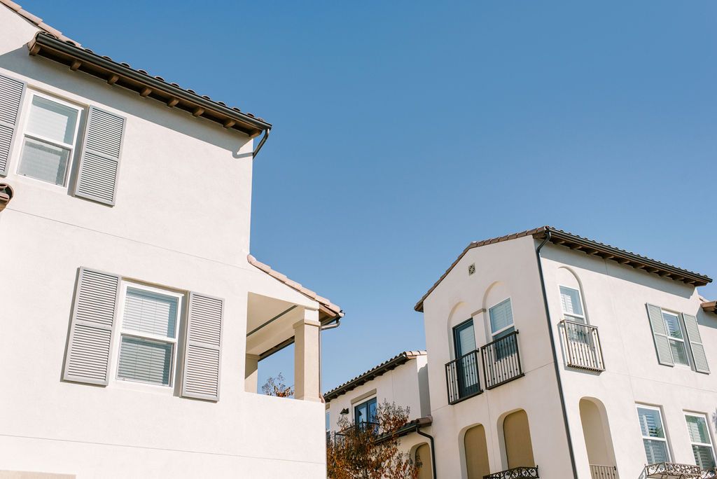 Two white houses with shutters on the windows are against a blue sky.