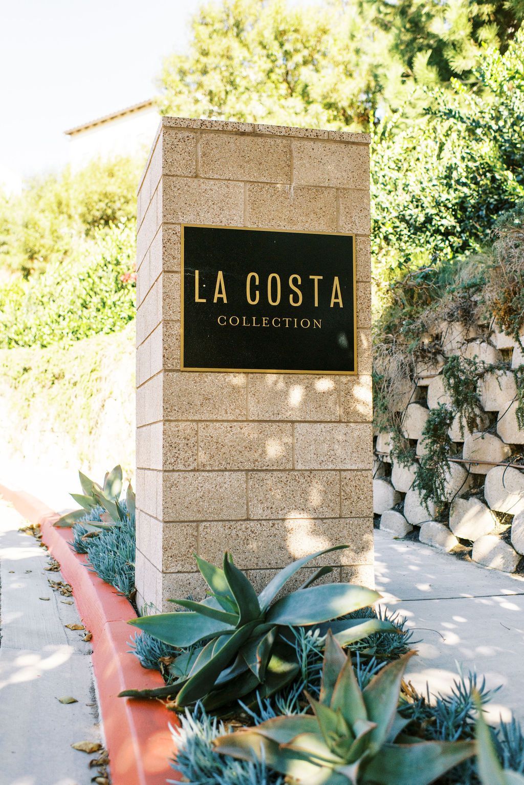 A sign for la costa collection is surrounded by plants.
