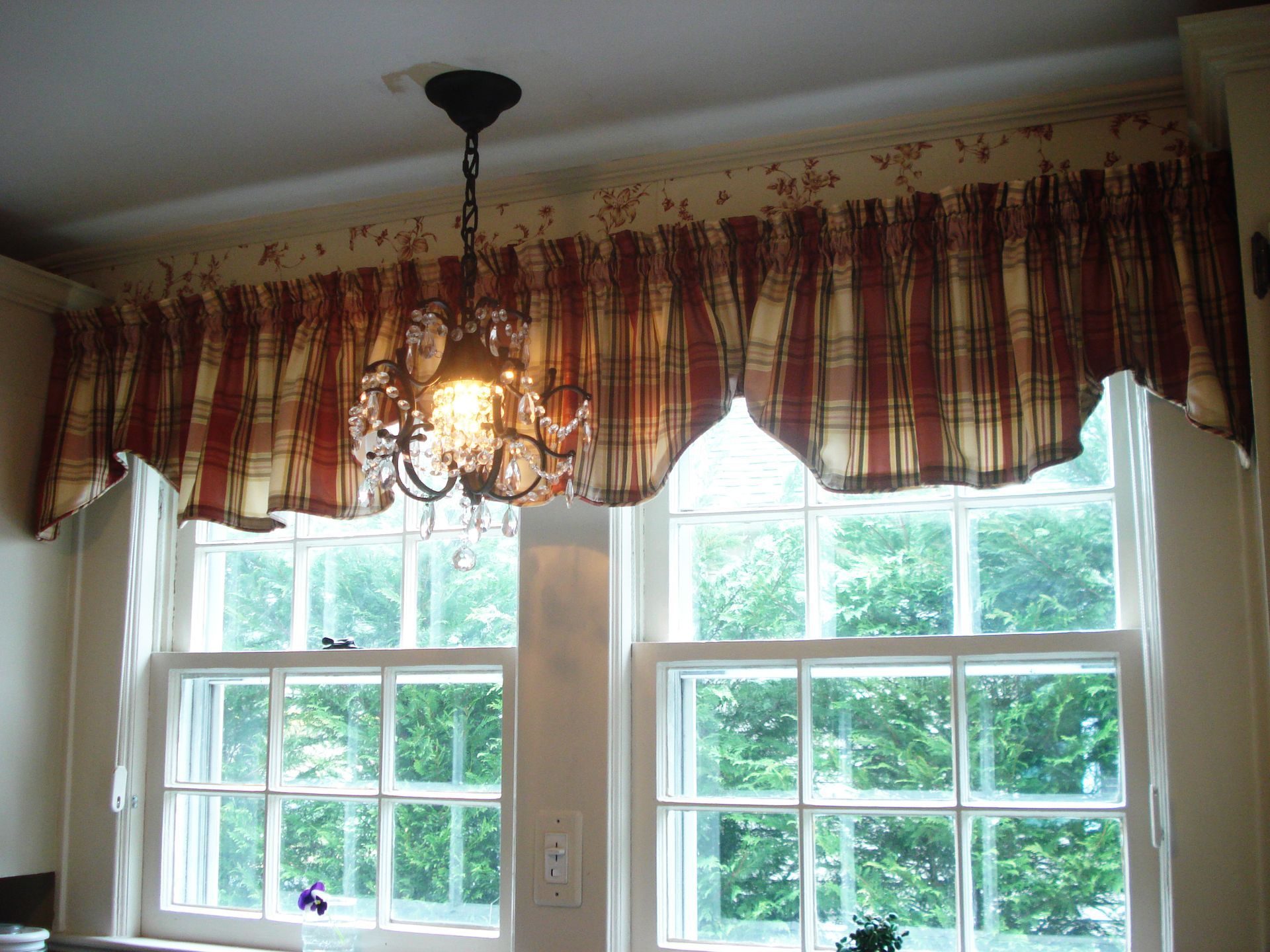 Two white-framed windows with a valance above, a chandelier hangs between.