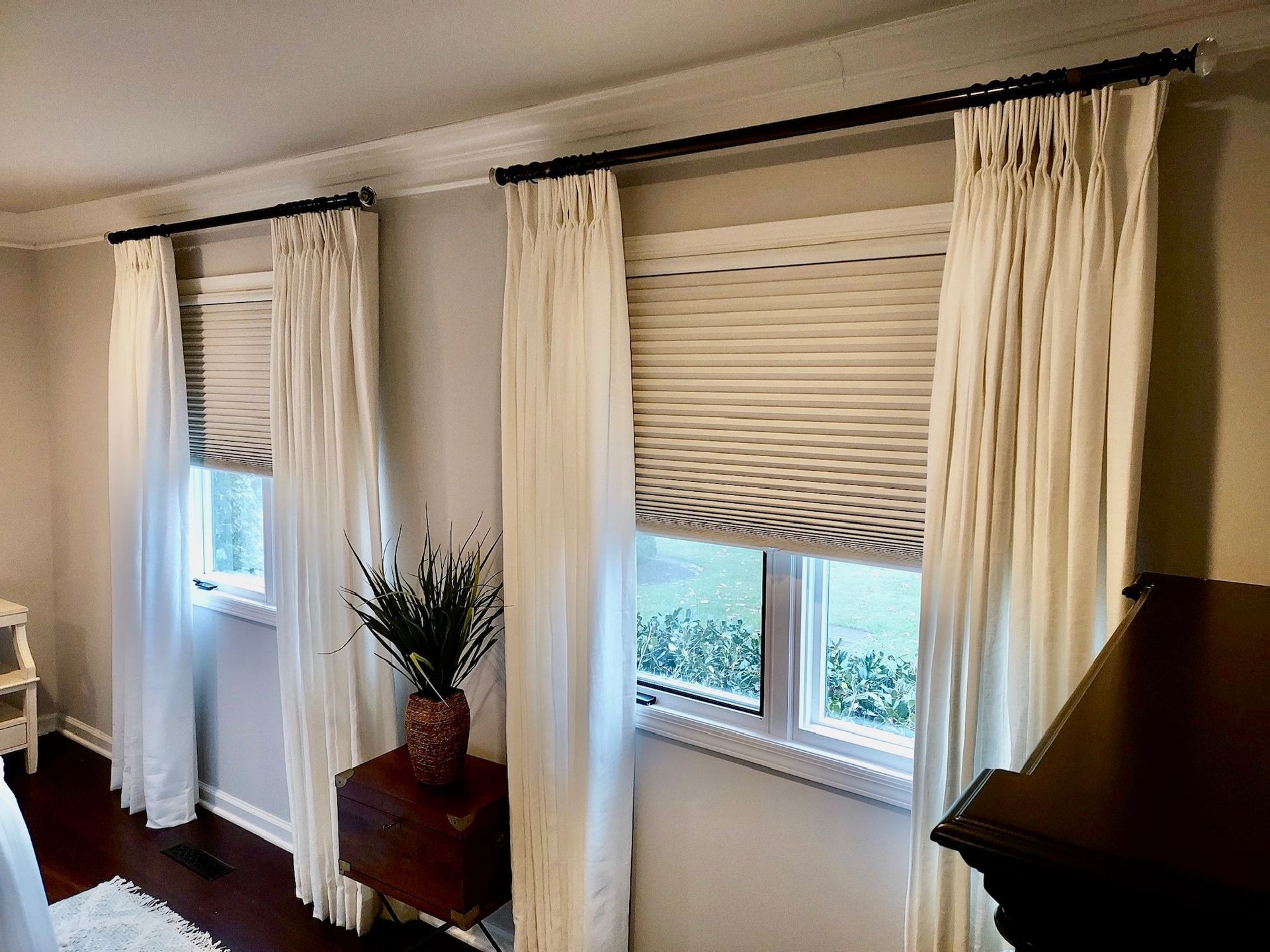 Two windows with sheer white curtains and shades, dark rods, dark dresser.