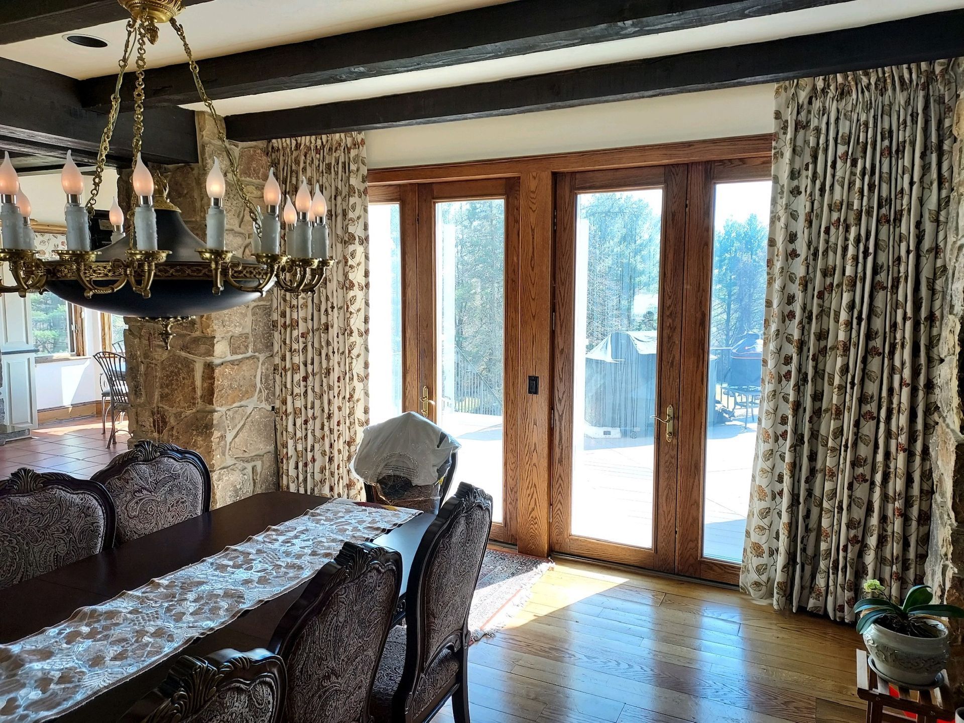 Dining room with long wooden table, patterned chairs, curtains, and large doors leading outside.