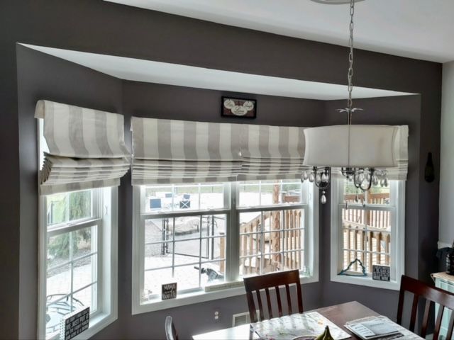 Dining room with gray striped Roman shades over a bay window, gray walls, and a chandelier.