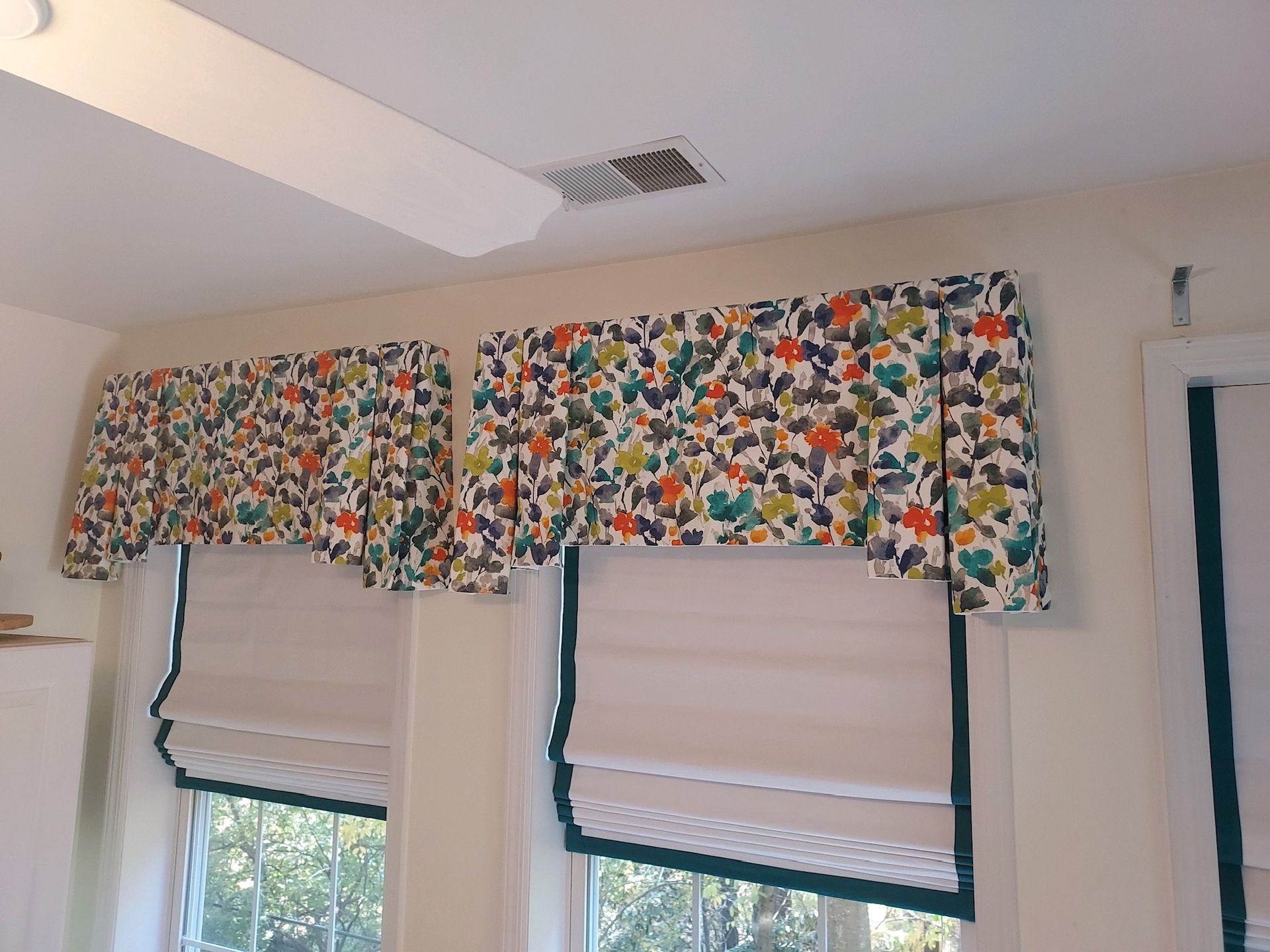Two windows with cream Roman shades, topped with floral valances, in a cream-colored room.