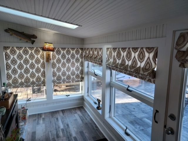 Sunroom with windows, paisley patterned shades, white trim, light-colored wood flooring, and ceiling.