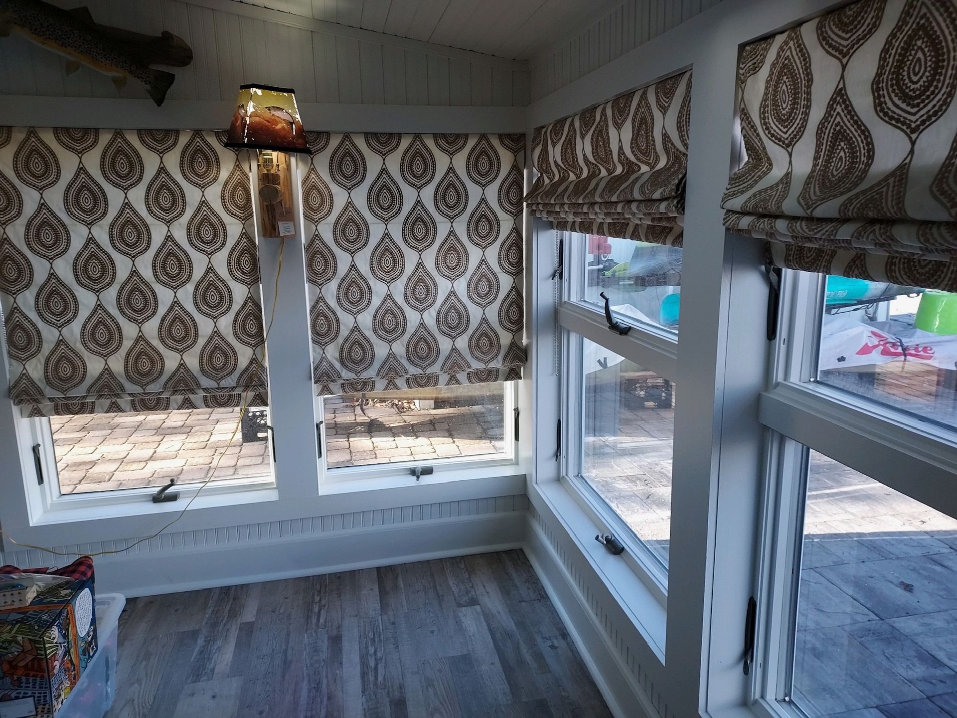 Sunroom with windows, brown patterned Roman shades, and wood floor.
