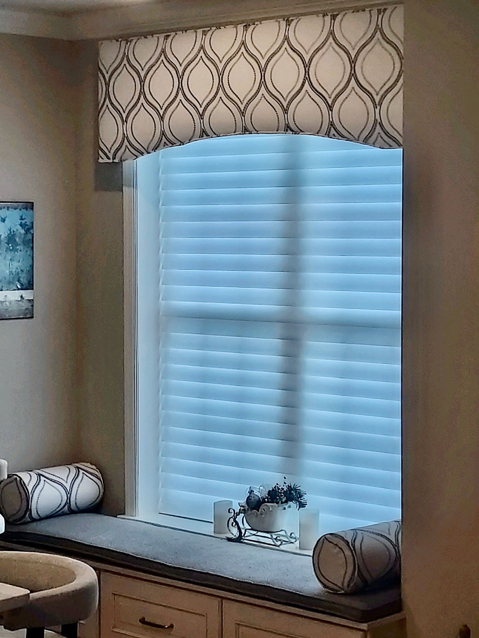 Window seat with white blinds, gray cushion, patterned valance, and decorative pillows.