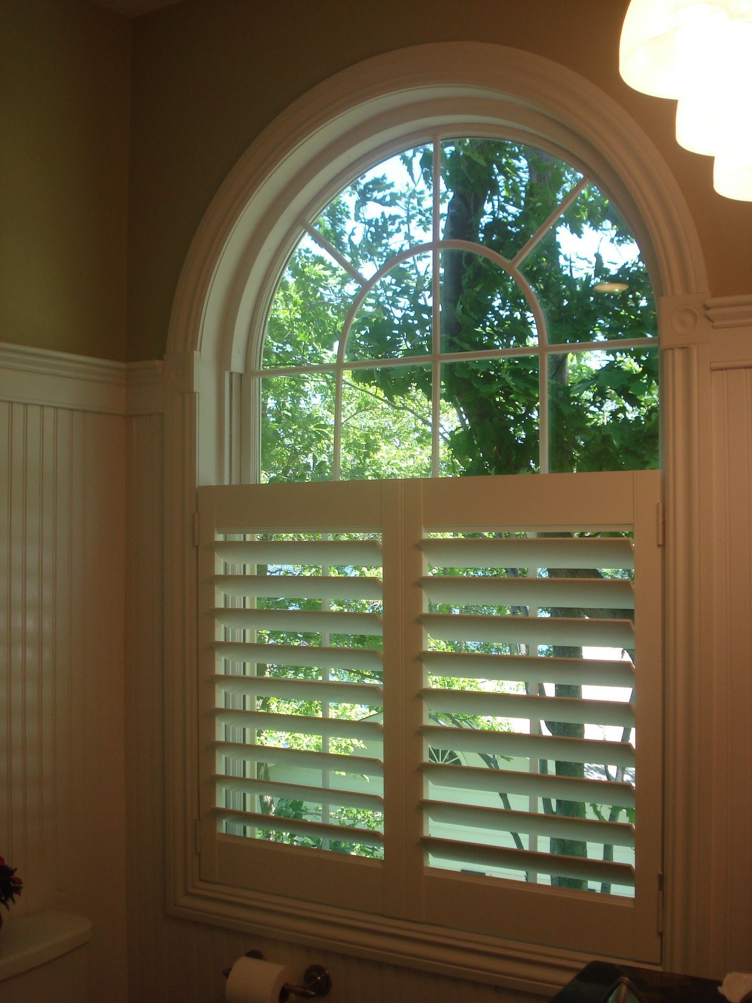 Arched window with white shutters, looking out at trees. The room has light green walls and white trim.