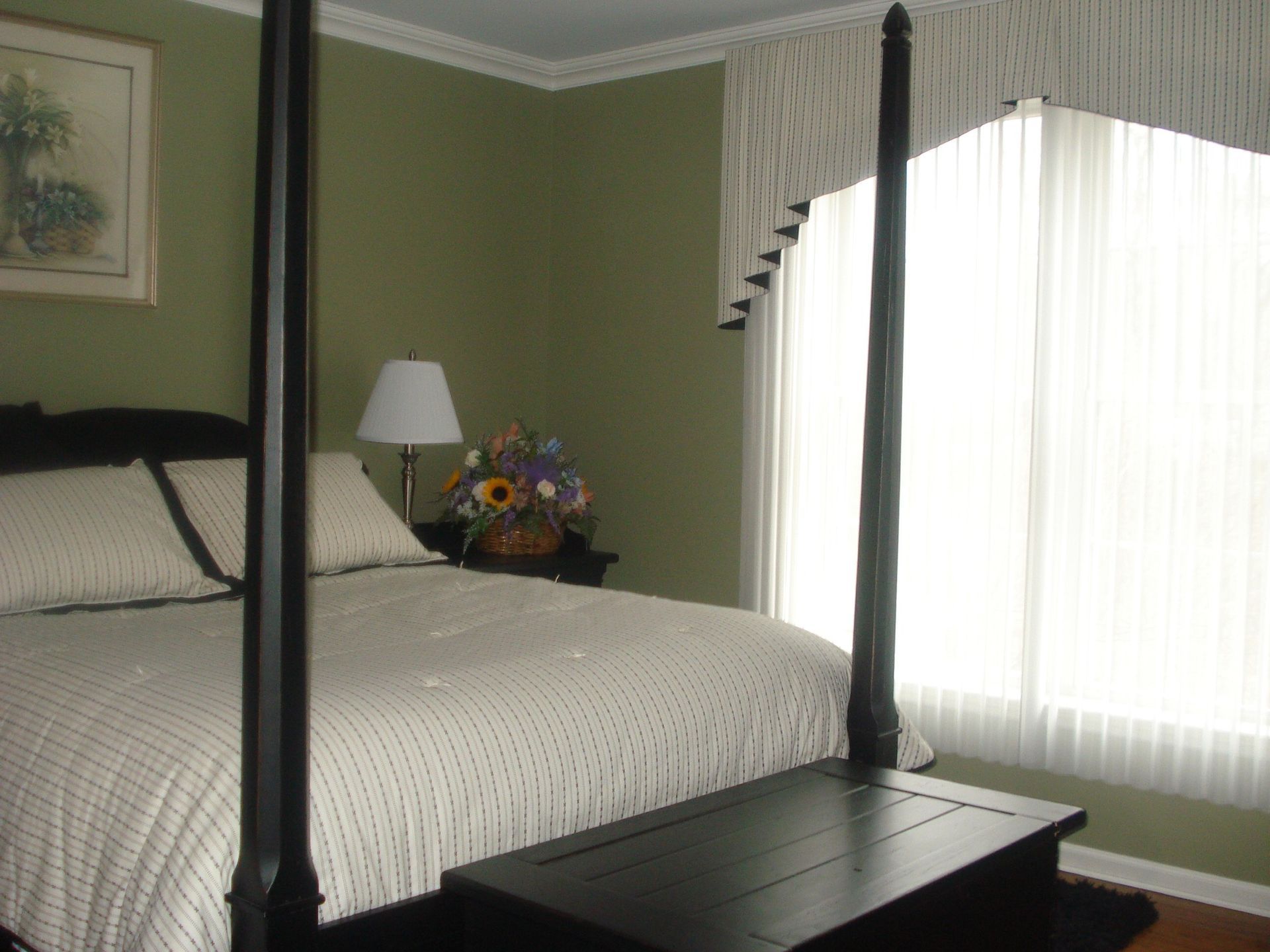 Bedroom with four-poster bed, green walls, sheer white curtains, and a decorative valance.