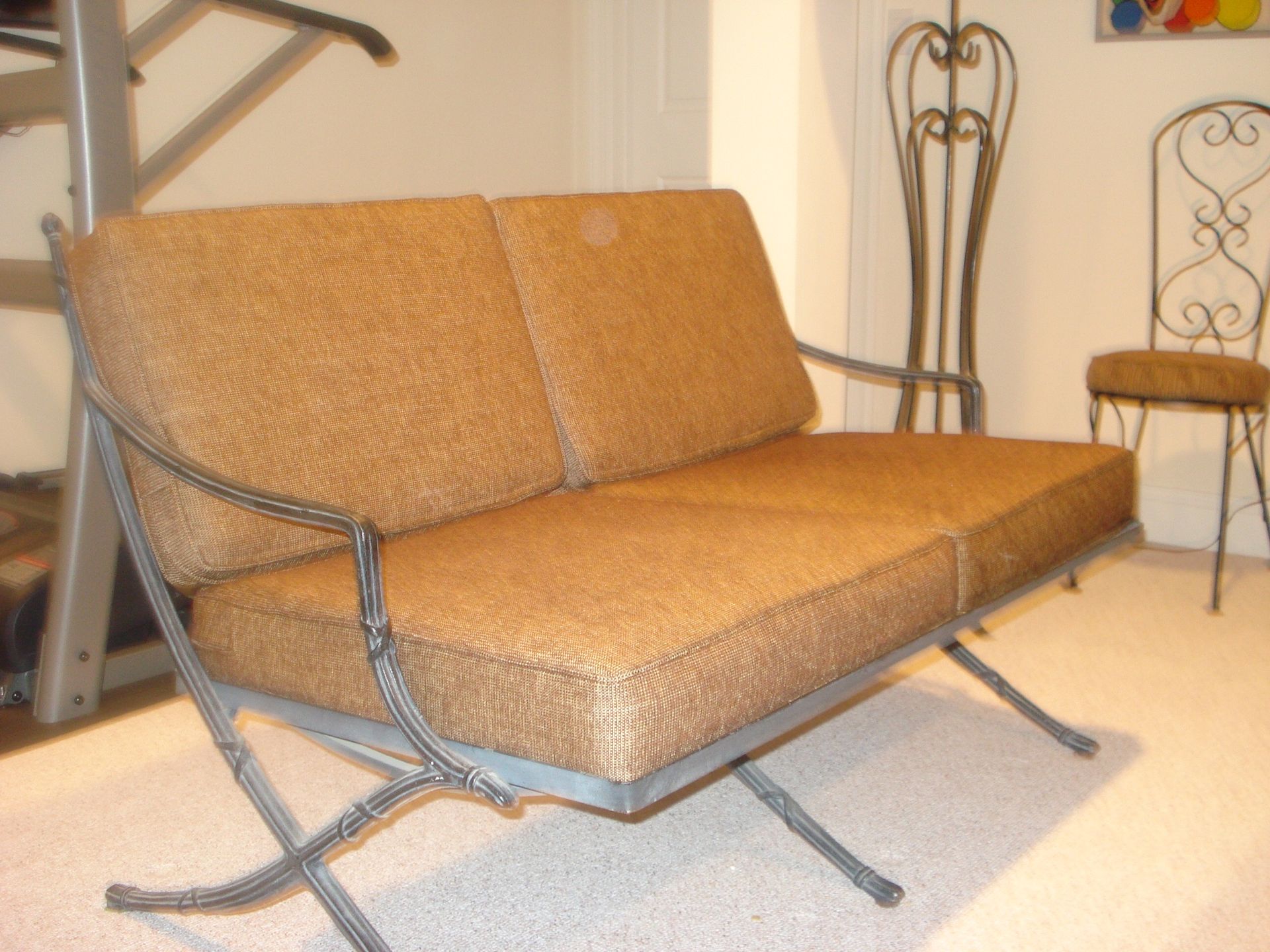 A two-seater sofa with brown patterned cushions and a gray metal frame, indoors.