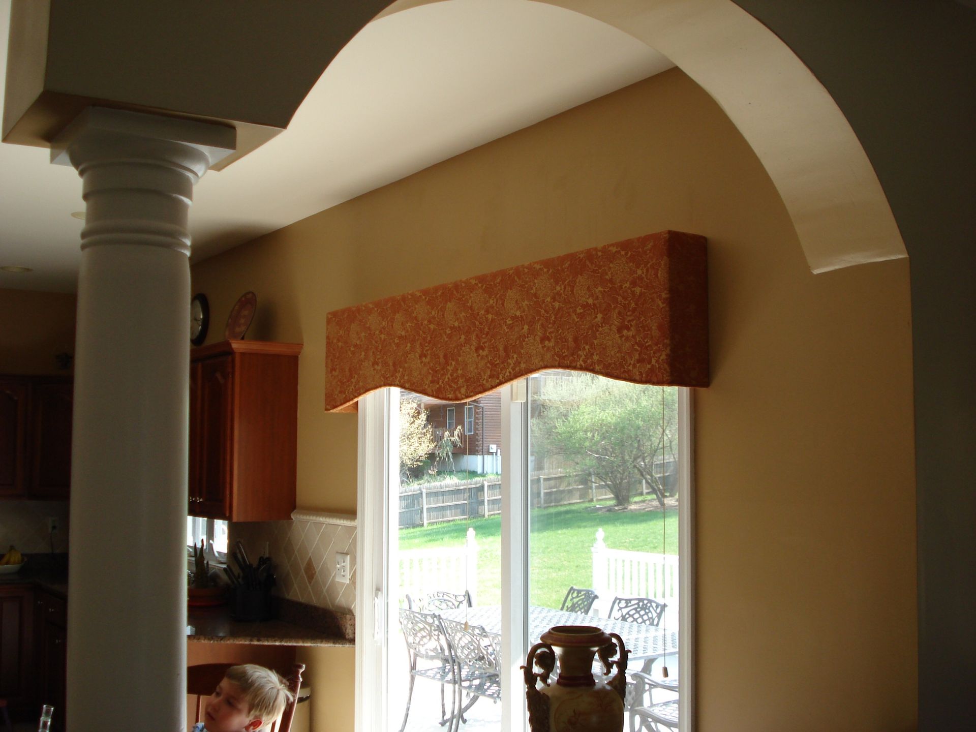 Arched doorway and window with orange valance. Tan walls and white columns.