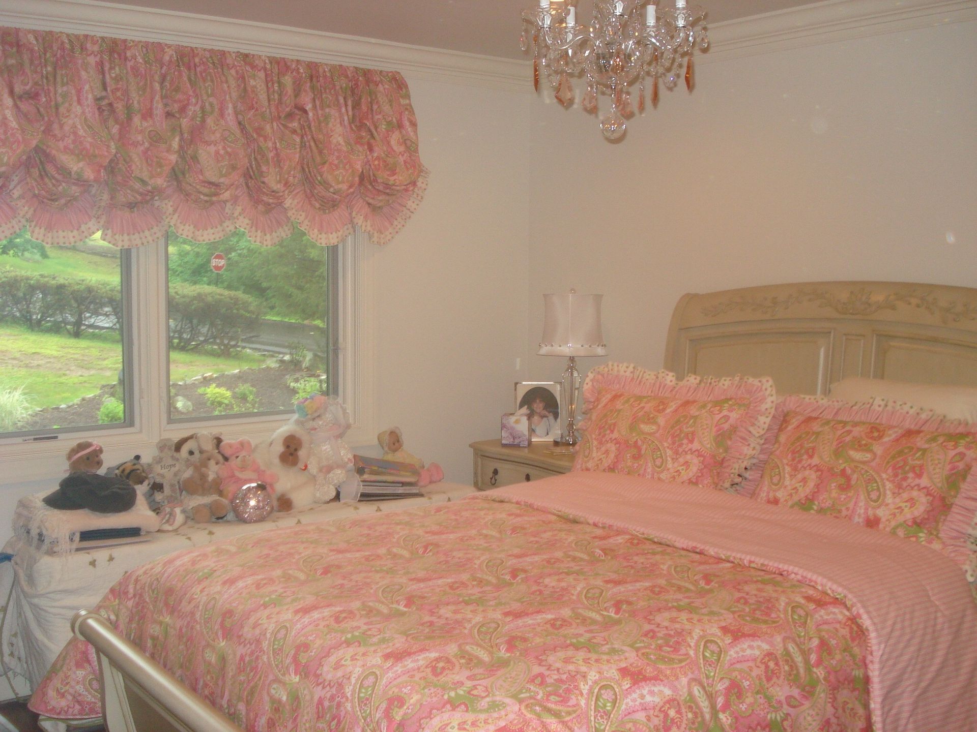 Pink bedroom with bed, window, ornate valance and a crystal chandelier.