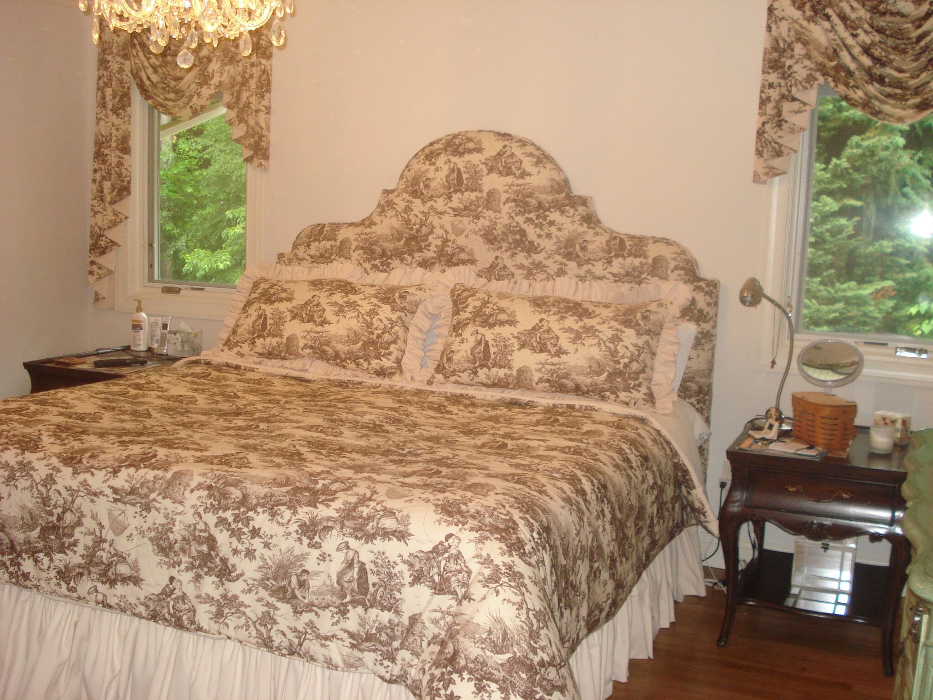 Bedroom with brown and white toile bedding, headboard, and curtains. Two windows, dark wooden bedside tables.