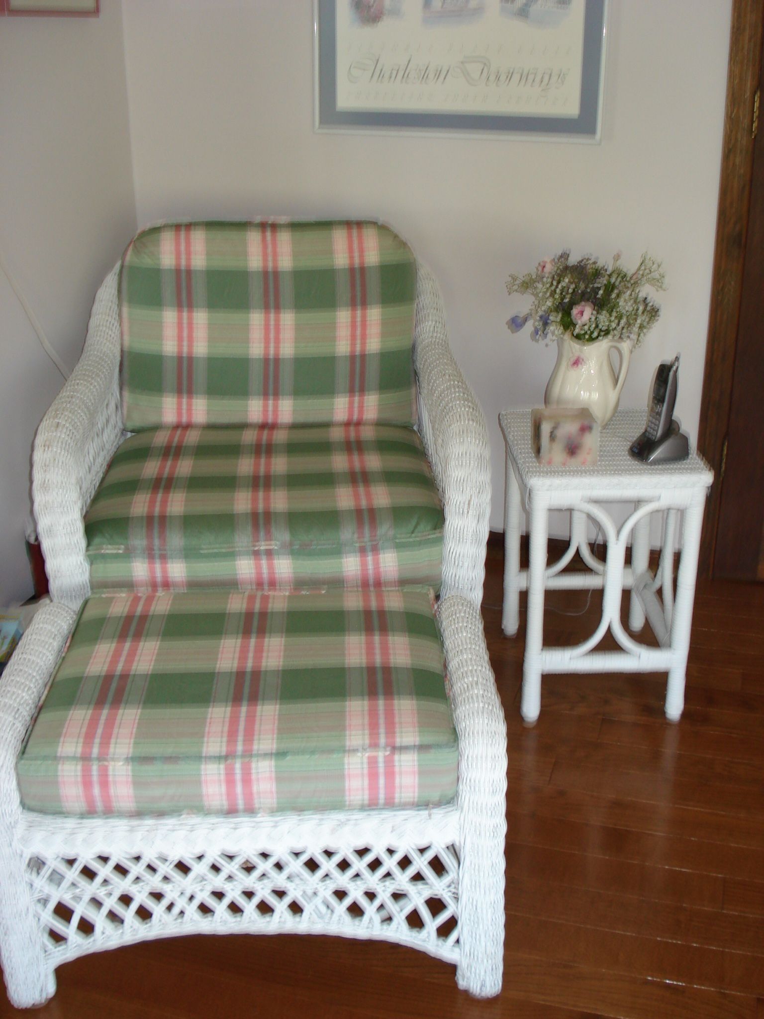 White wicker chair and ottoman with plaid cushions, next to a small table with flowers.