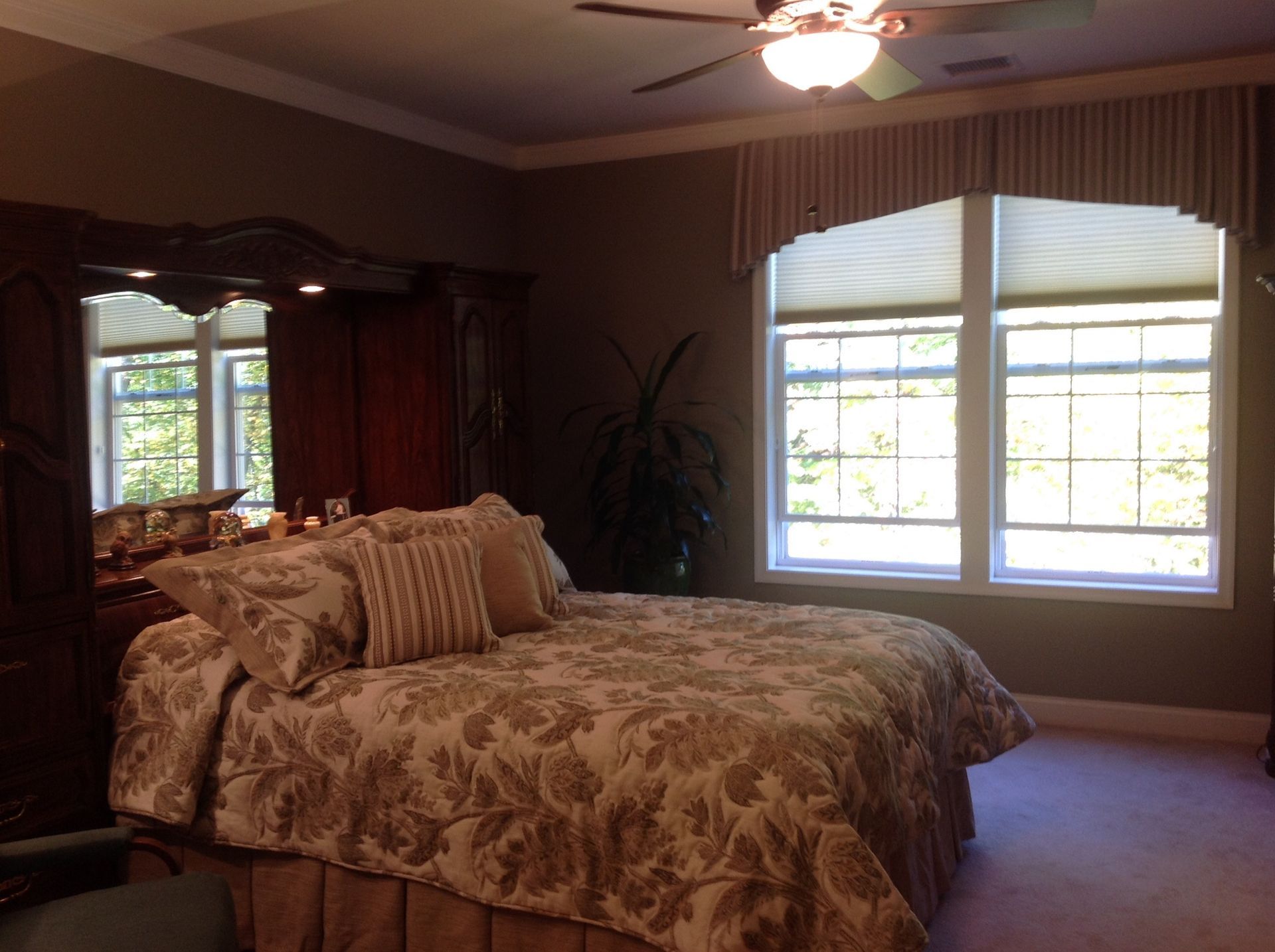 Bedroom with bed, dark wood armoire, windows with shades, and a decorative valance.