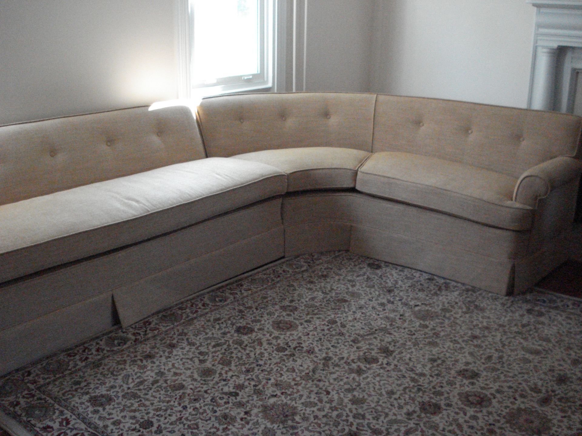 Beige sectional sofa in a room with a floral patterned rug and a window.
