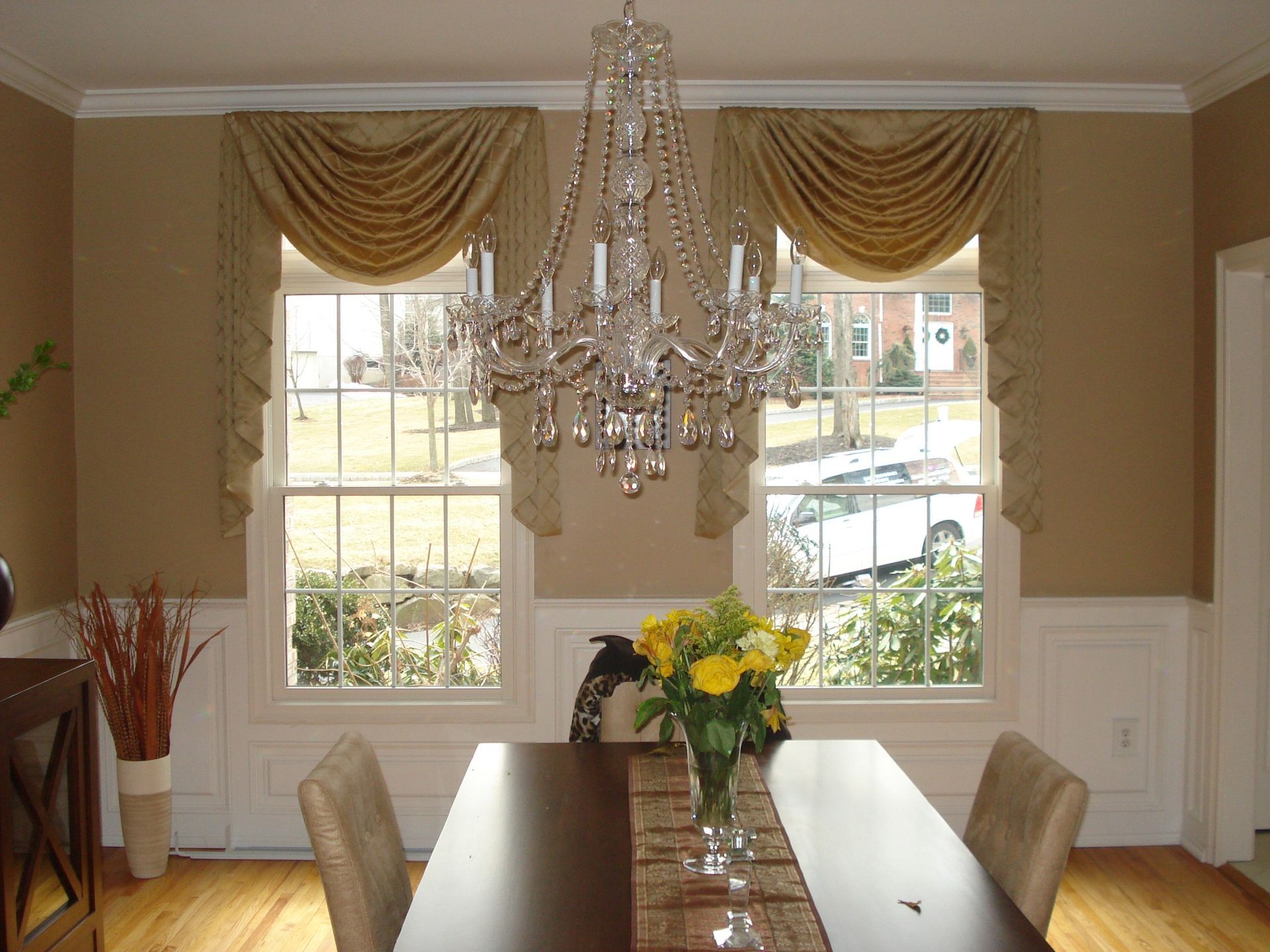 Dining room with chandelier, windows with draped curtains, table set with flowers.