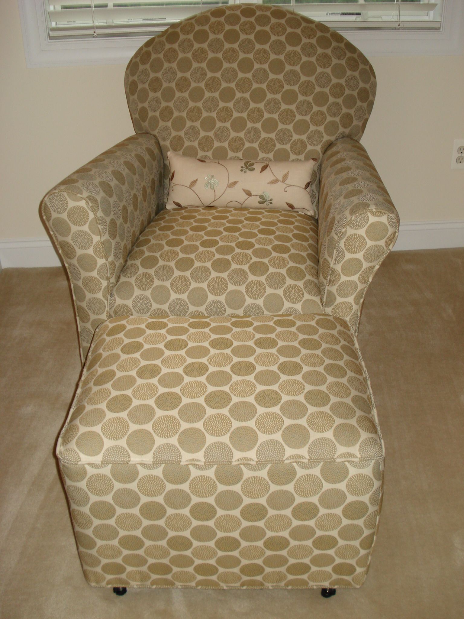 Upholstered armchair and ottoman with a geometric pattern in tan and cream, with a small pillow on seat.