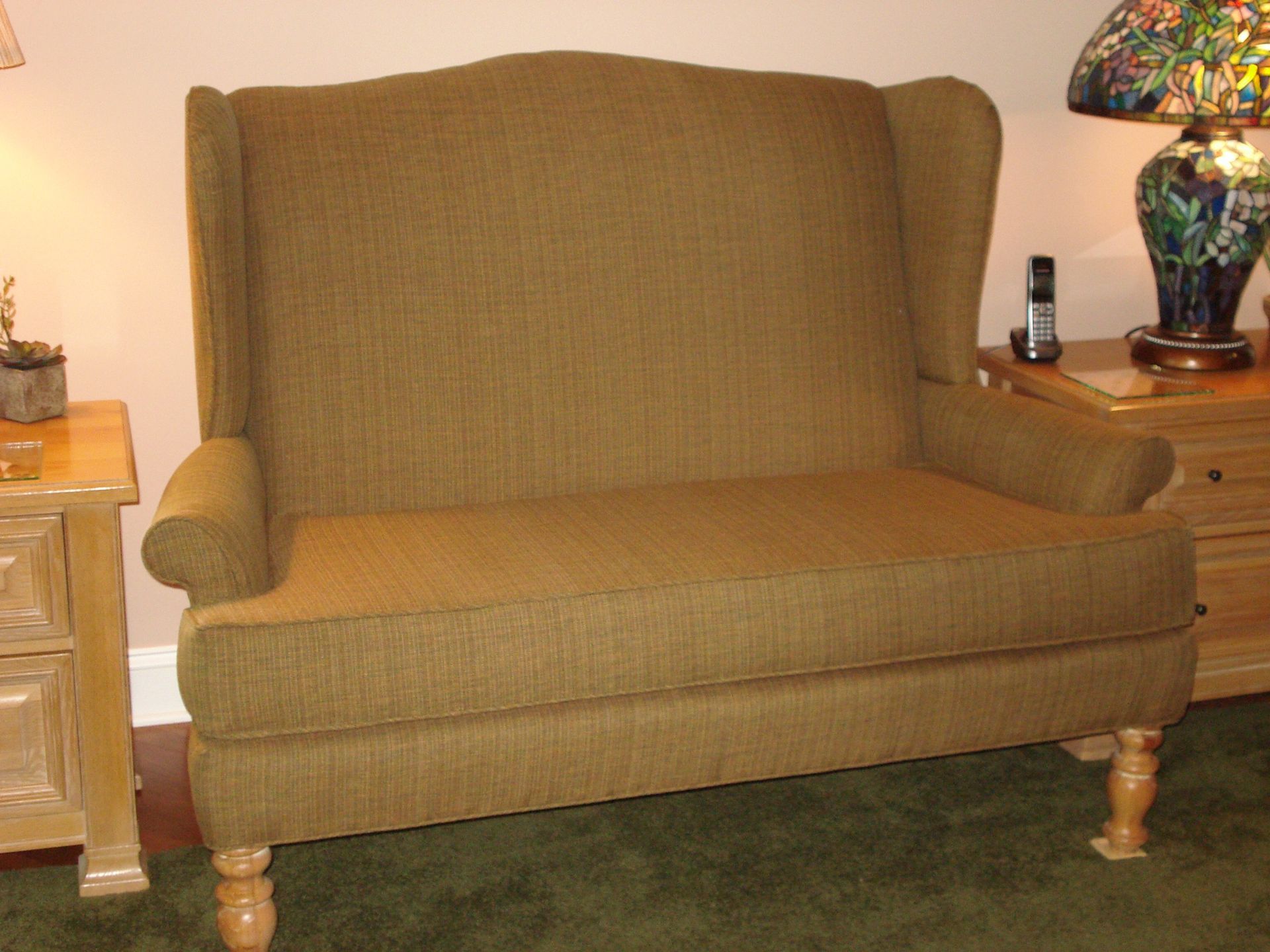 Green upholstered loveseat with high back and roll arms in a room with a lamp on a table.