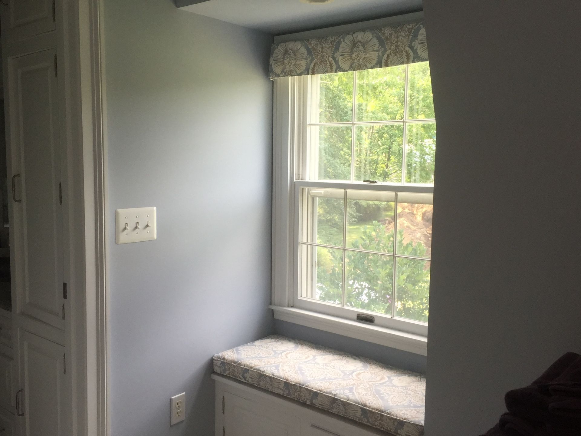 A small window seat in a blue room with a floral valance and cushion.