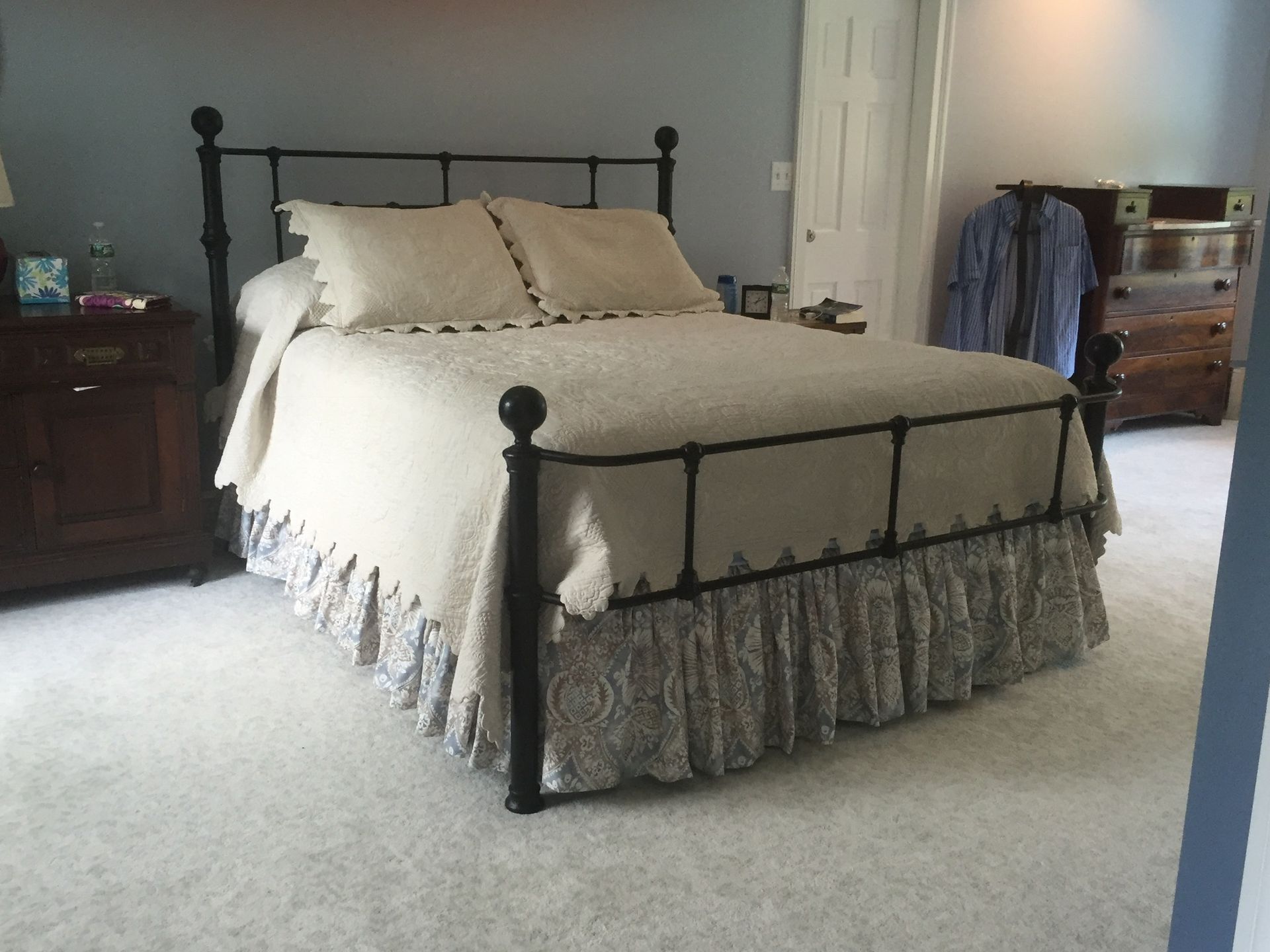 Bedroom with a black metal bed, cream bedding, and floral bed skirt. Features a dresser and carpet.