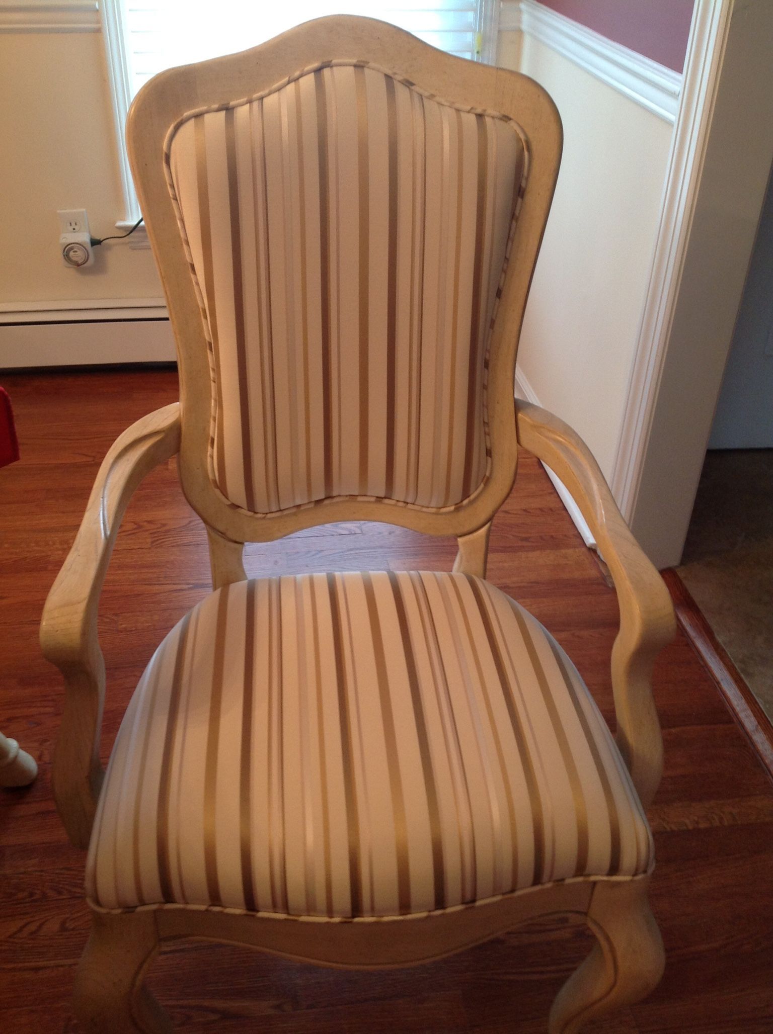 Beige striped upholstered chair with curved arms and back, on a hardwood floor.