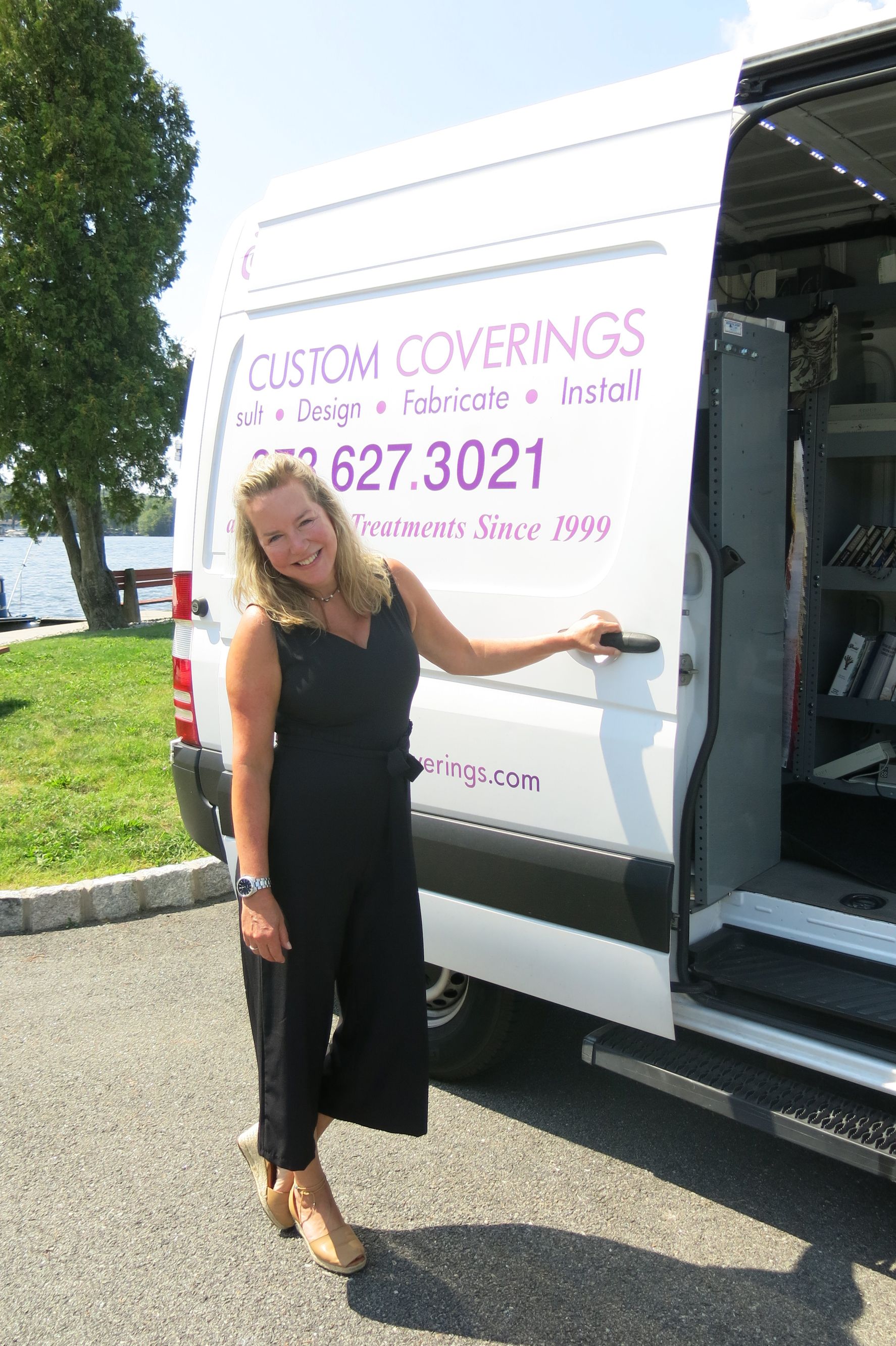 Woman in black jumpsuit stands next to a white van with 