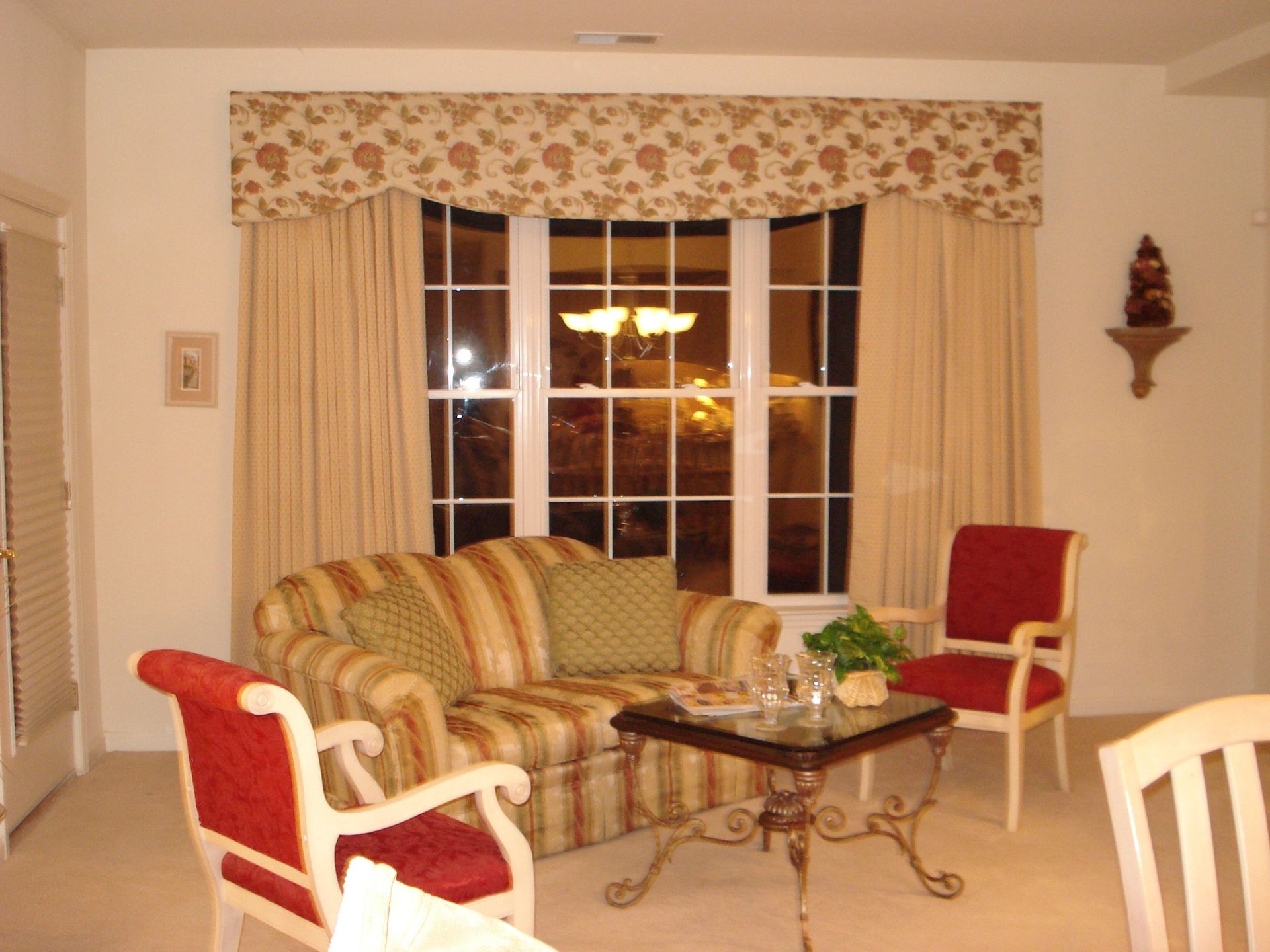 Living room with striped sofa, red chairs, bay window with floral valance, and small table.