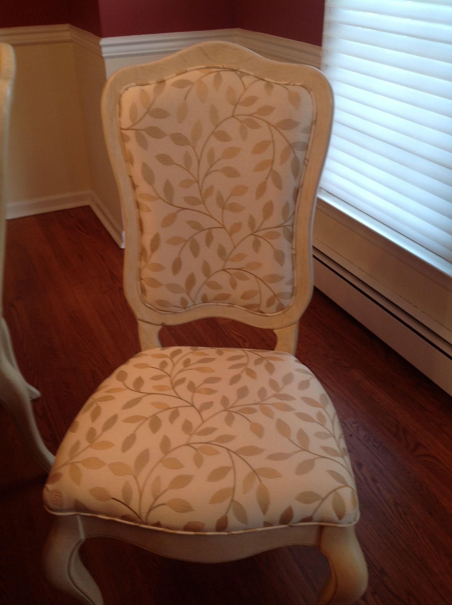 Cream-colored dining chair with beige leaf-patterned fabric, set on a wood floor near a window.