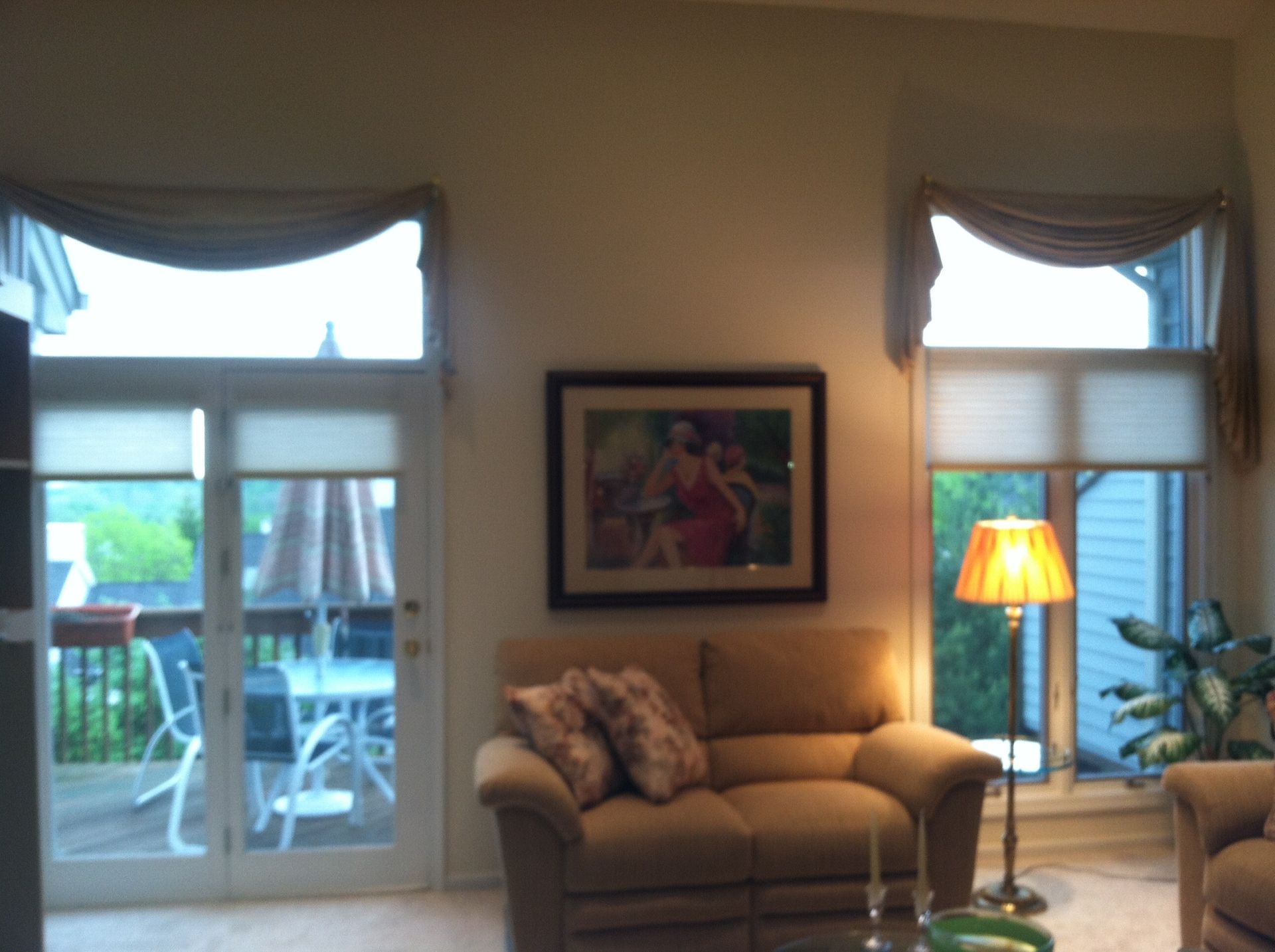 Living room with beige sofa, framed art, and windows with drapes overlooking a deck.