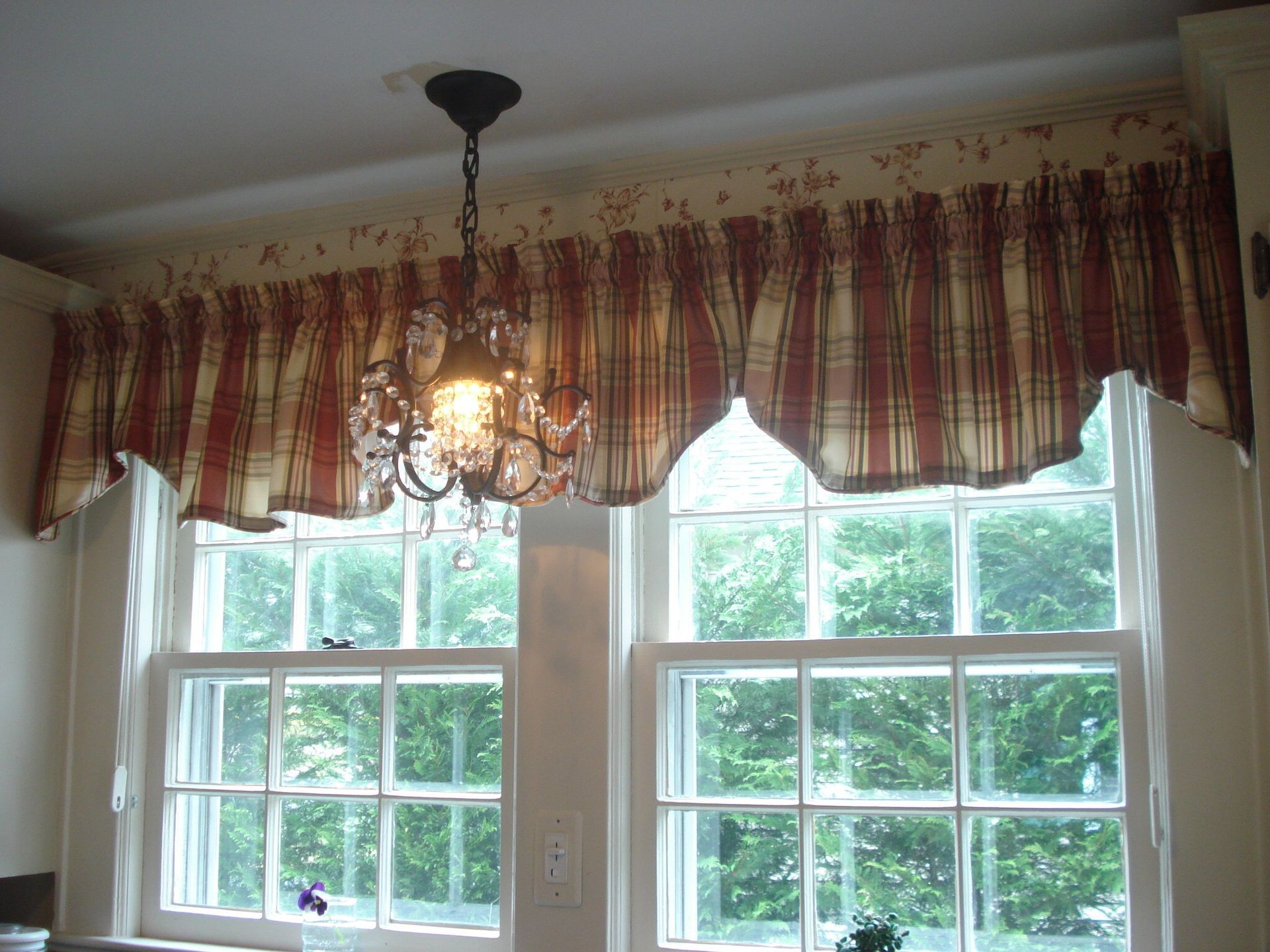 Red and cream striped valance over two white-framed windows with a chandelier hanging in front.