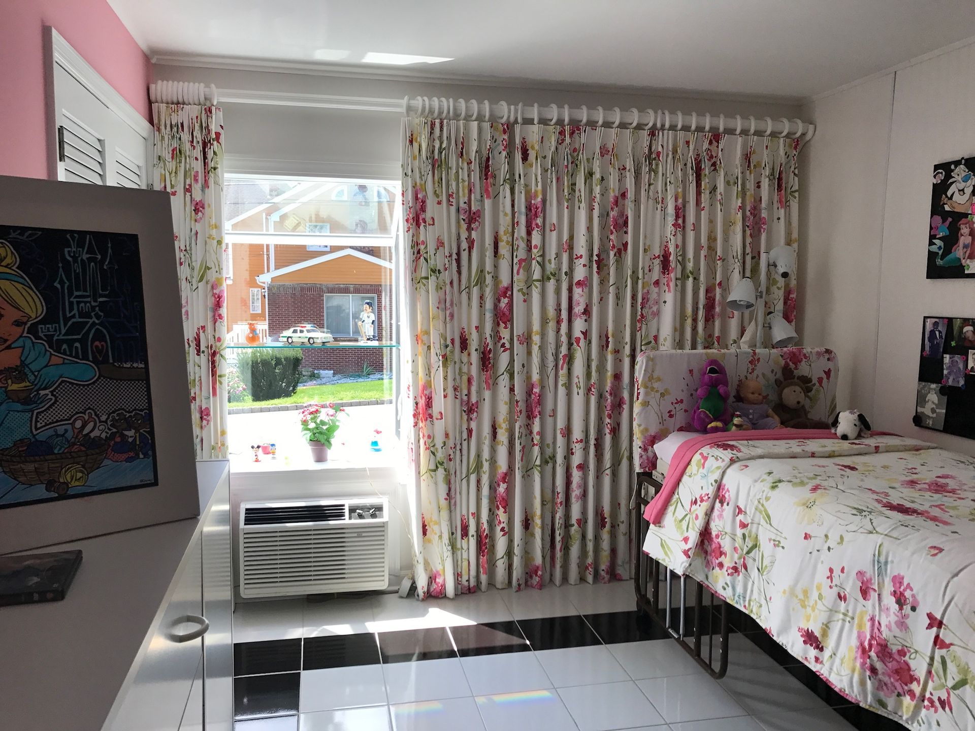 A girl's bedroom with floral curtains, bedding, and decor. Window view, white walls, pink accents.