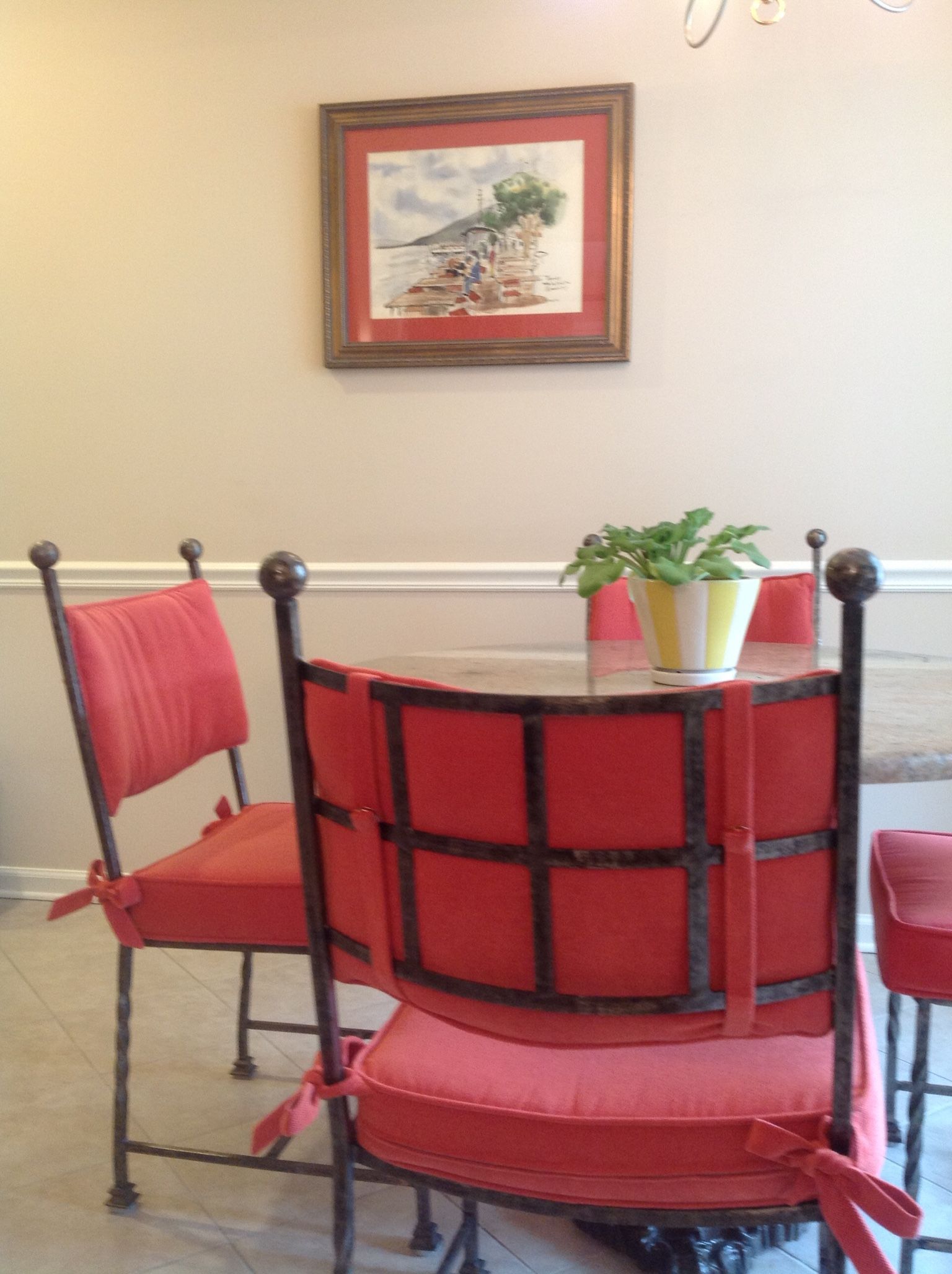 Red chairs around a glass table, with a framed painting and potted plant.