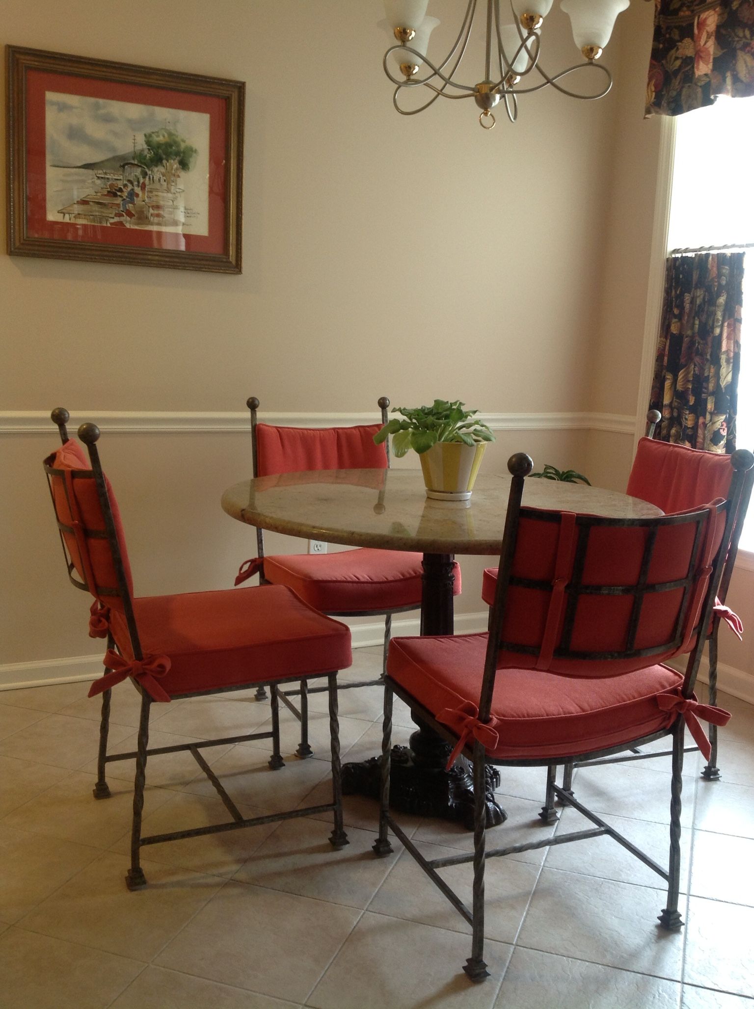 Dining table with red cushioned chairs, art on wall, and a plant.