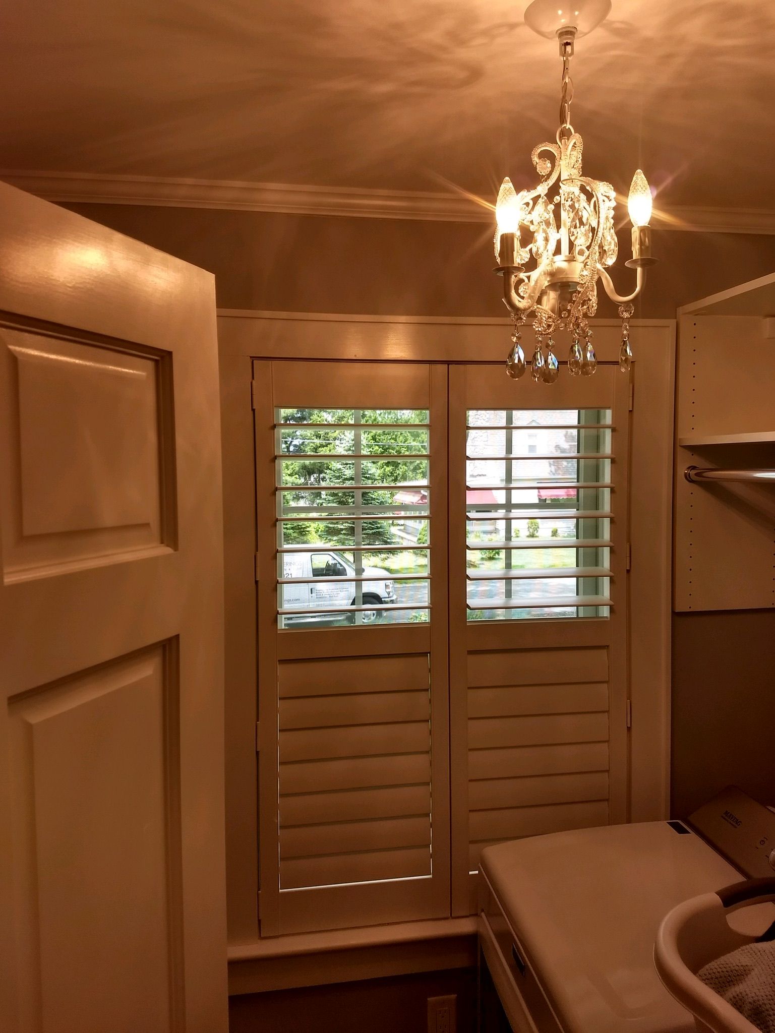 Laundry room with open window shutters, chandelier, white door.