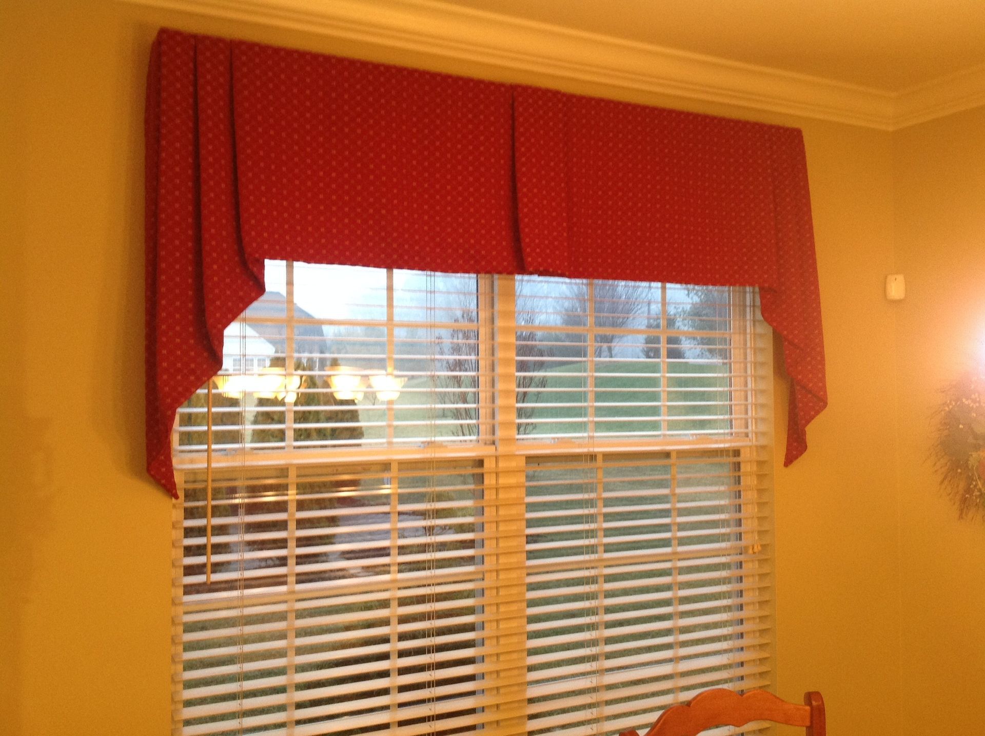Red polka dot window valance over a window with blinds, set in a room with beige walls.