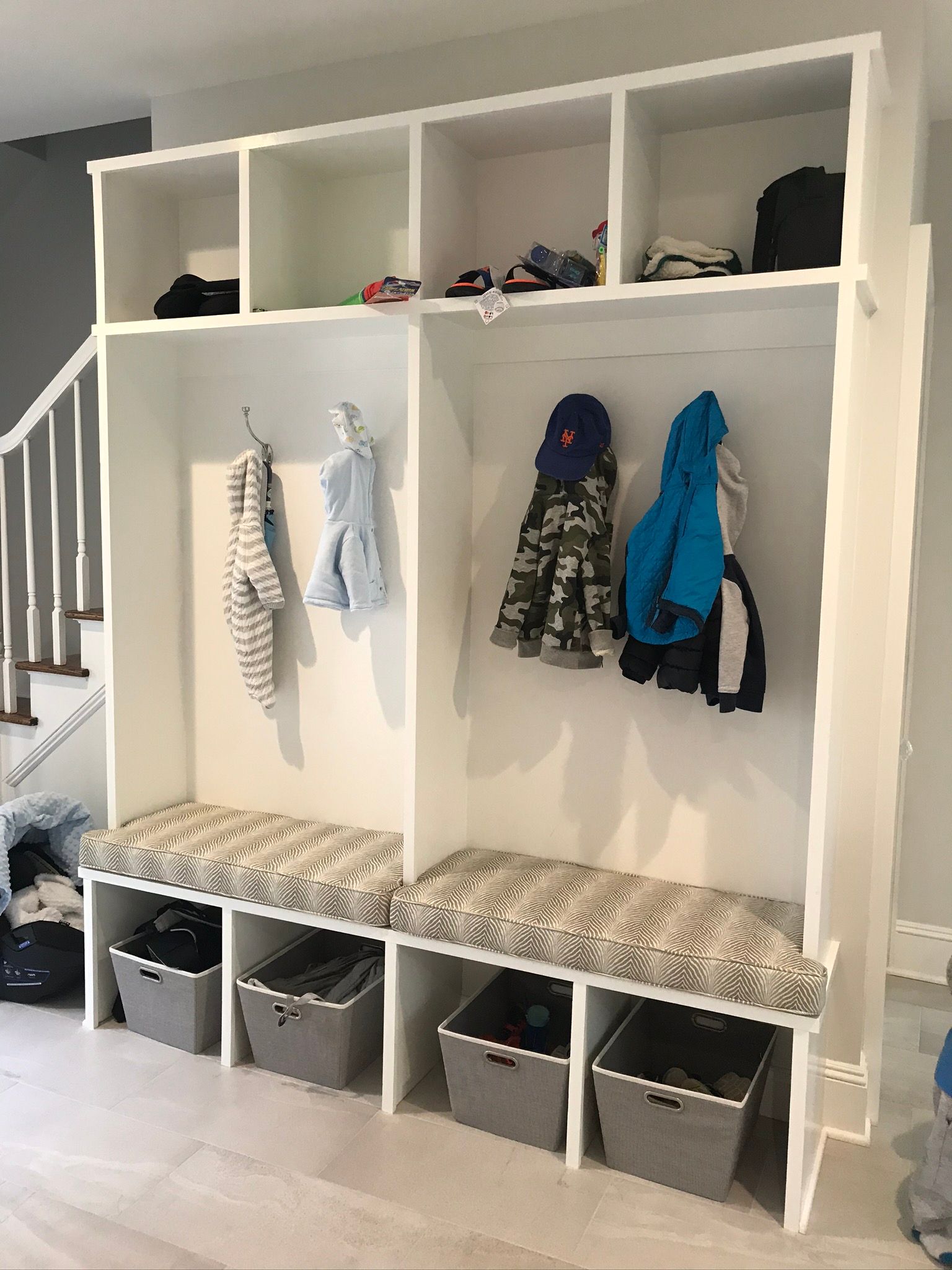 White built-in entryway organizer with benches, storage bins, and coat hooks under upper storage.