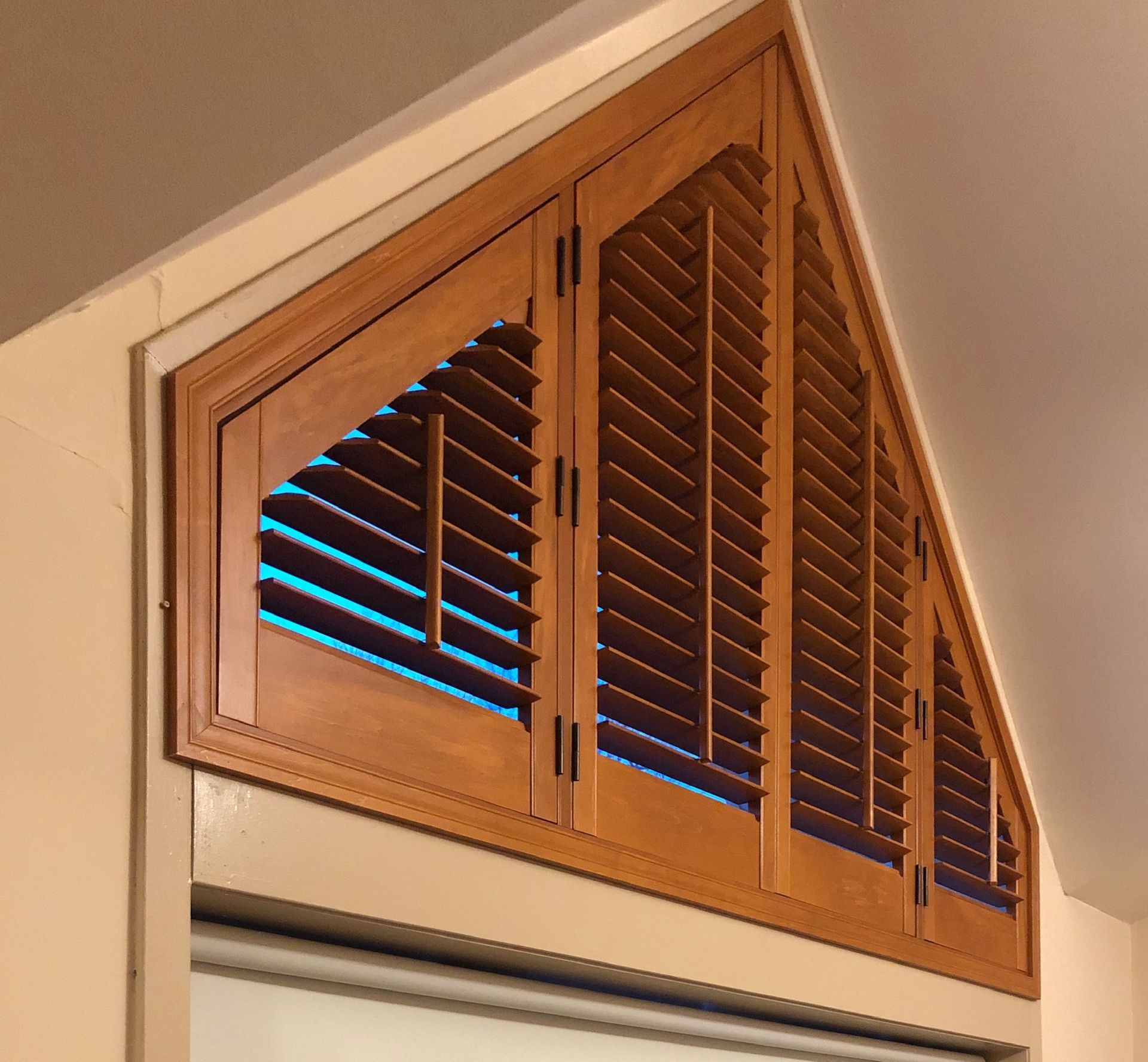 Triangular wood shutters above a window, brown wood with open louvers.