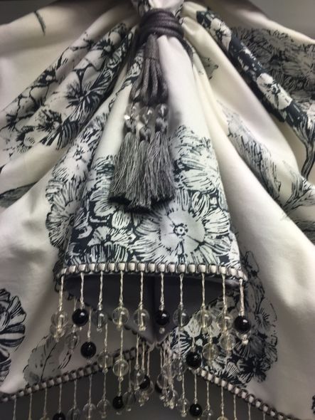 Close-up of a white curtain with a black floral print and a beaded tassel.