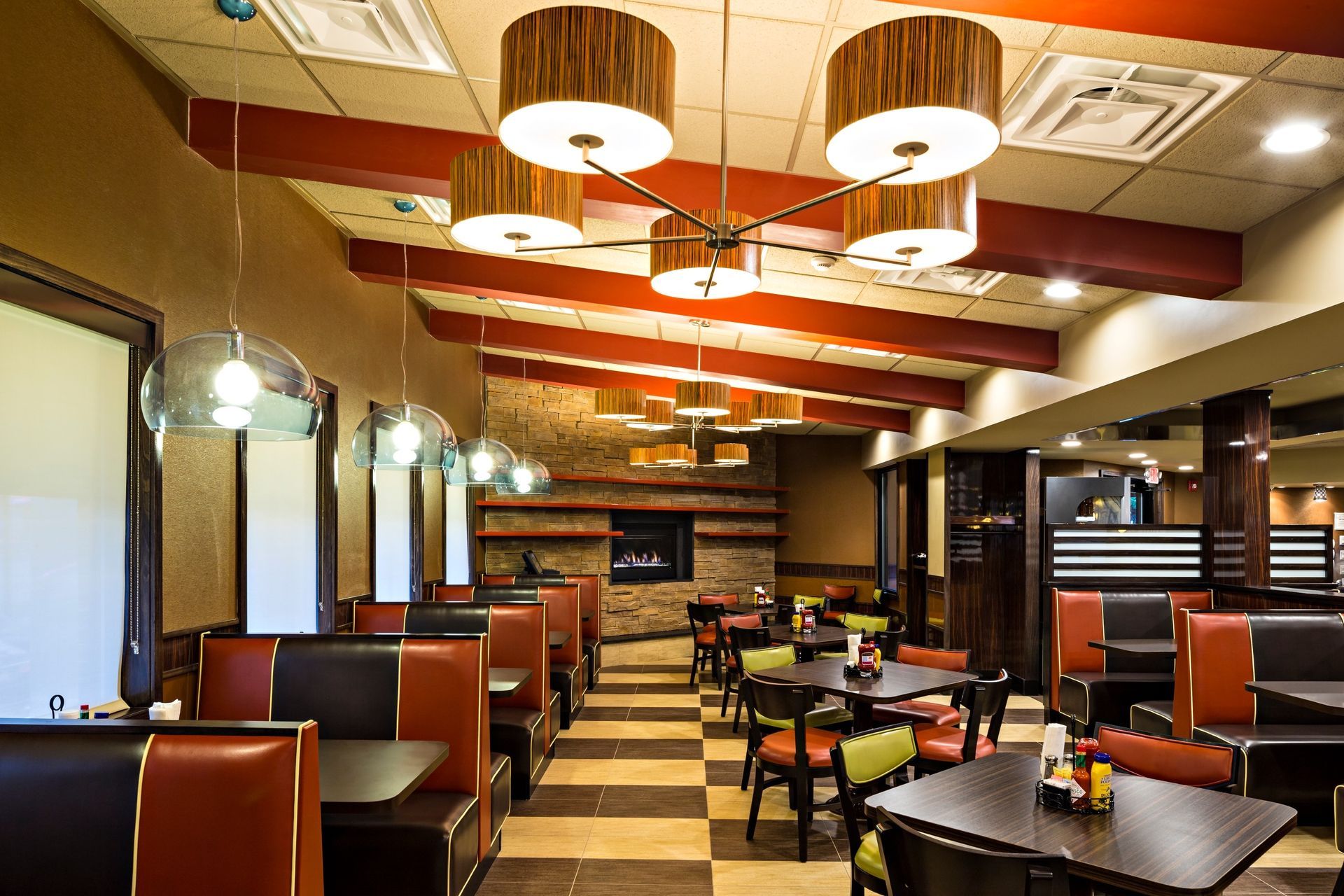 Restaurant interior: booths and tables with red and black seating, checkered floor, fireplace, patterned ceiling lights.