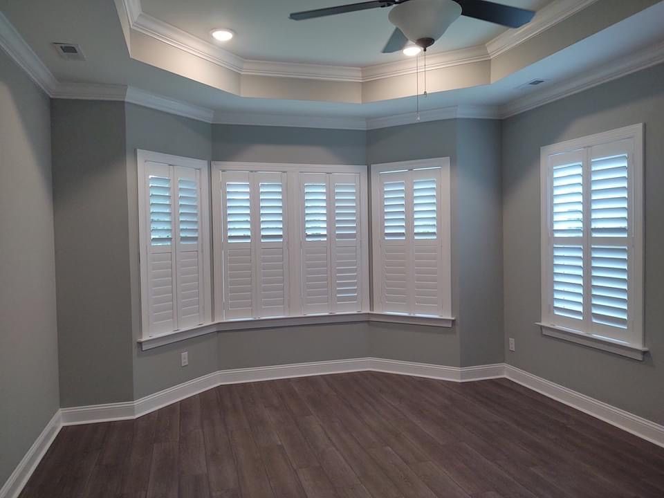 Gray-walled room with white shutters and wood flooring. A ceiling fan and recessed lights are visible.
