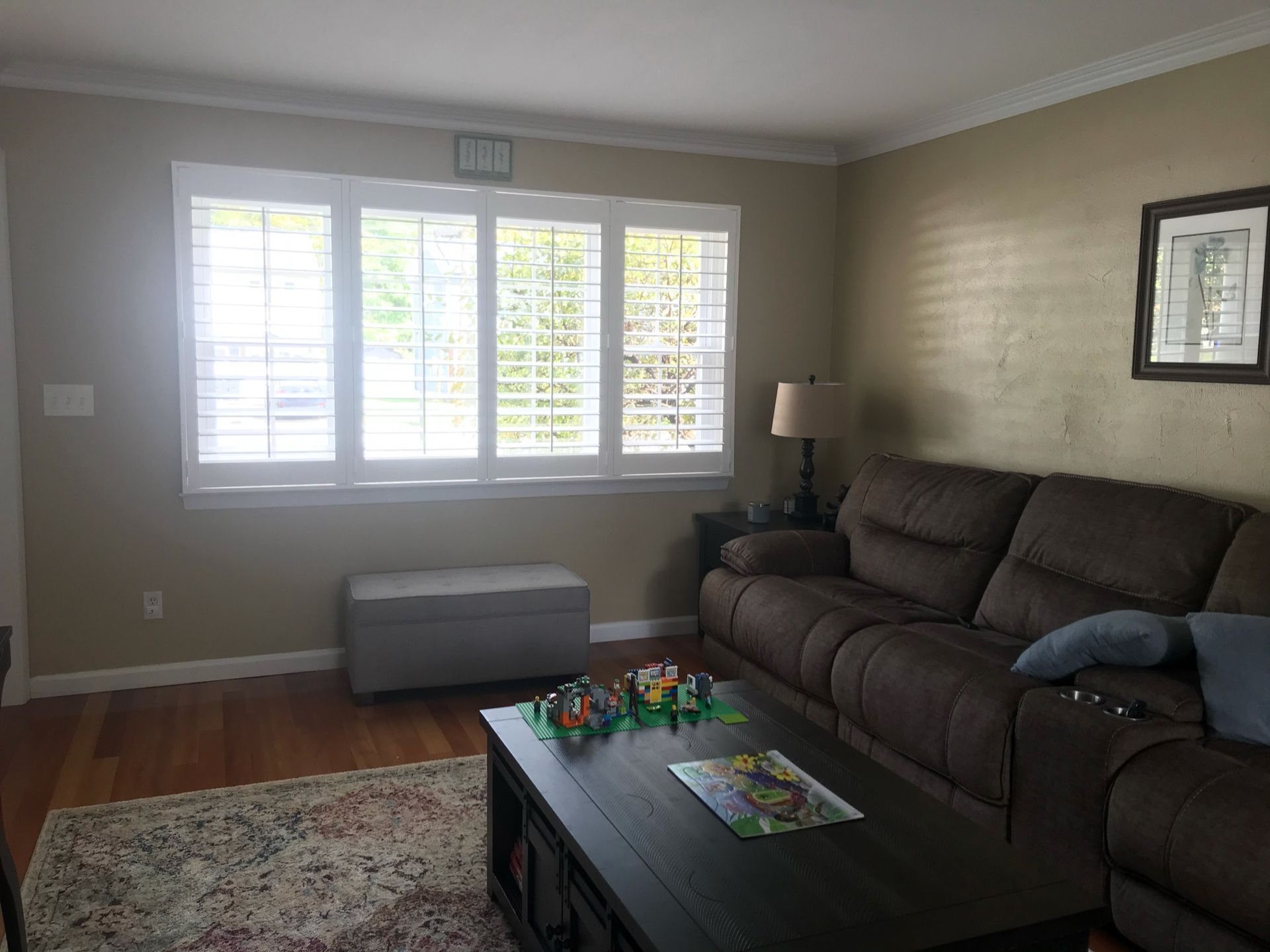 Living room with brown sofa, shutters, and coffee table with toys on rug.