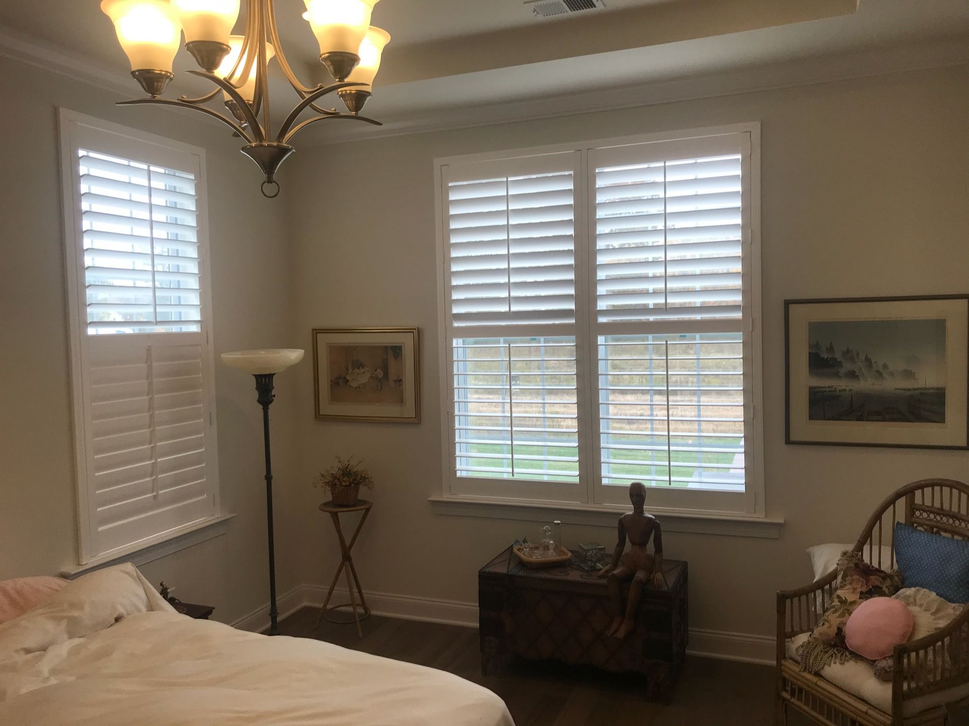 Bedroom with white shutters, art, furniture, and a chandelier.